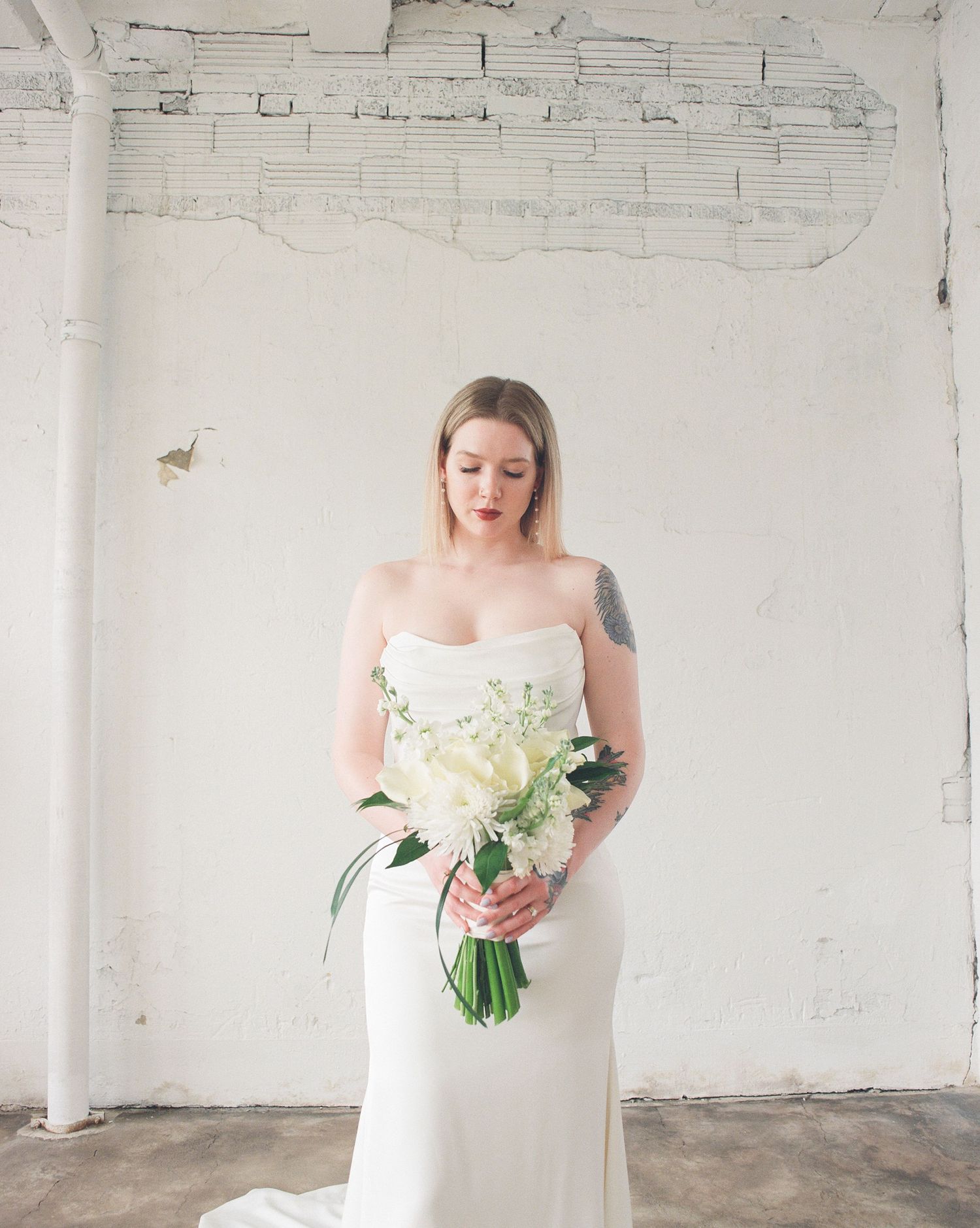 Classic bridal portraits in strapless white gown holding romantic bouquet in industrial space.