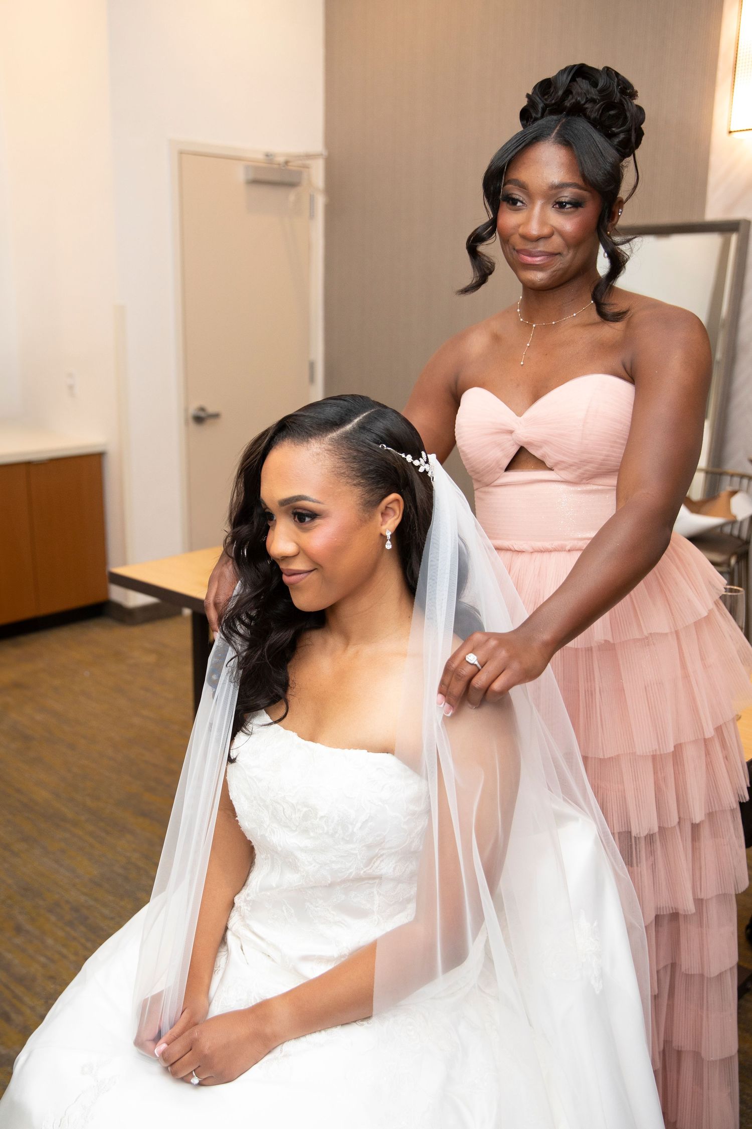 Wedding preparation scene with bridesmaids in pink dresses helping with the bridal veil.