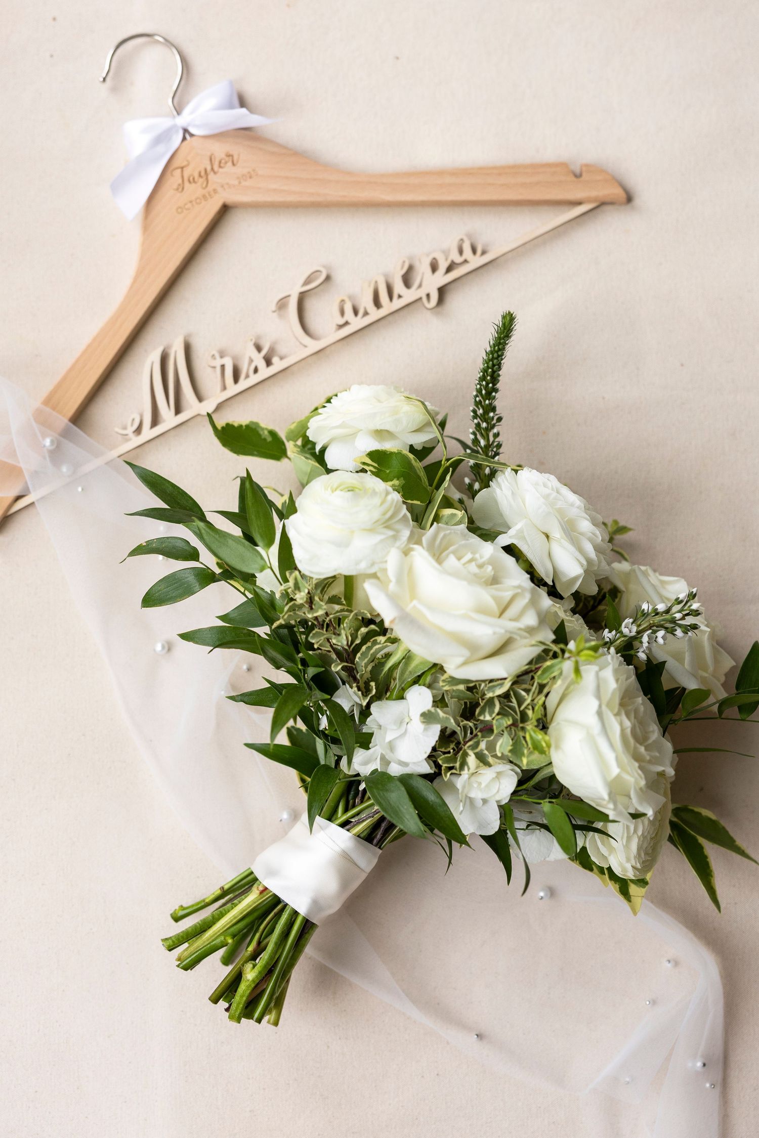 White rose bouquets displayed on personalized wooden hangers with greenery accents.
