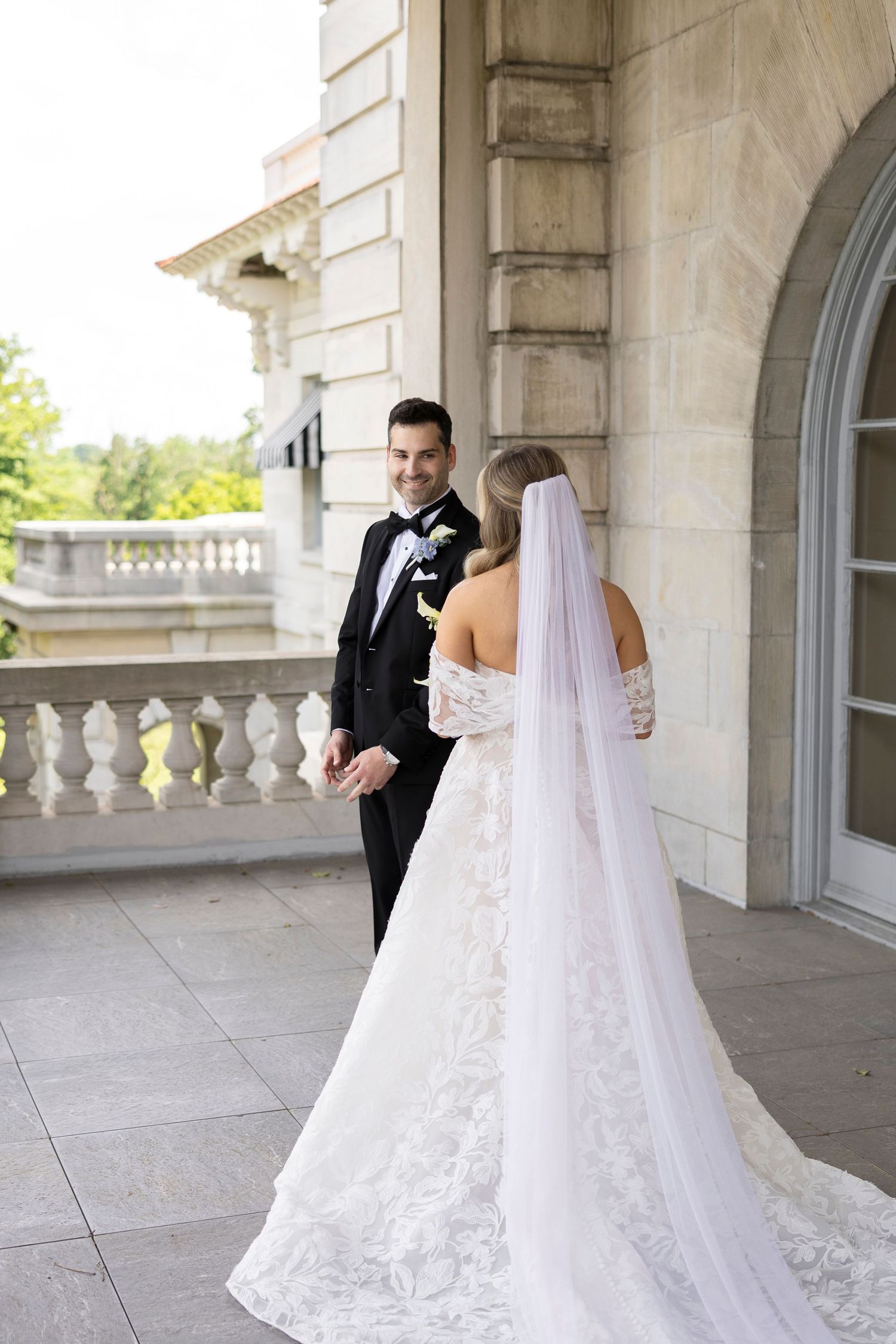 Romantic first look moment between newlyweds on a grand stone terrace with arched windows.