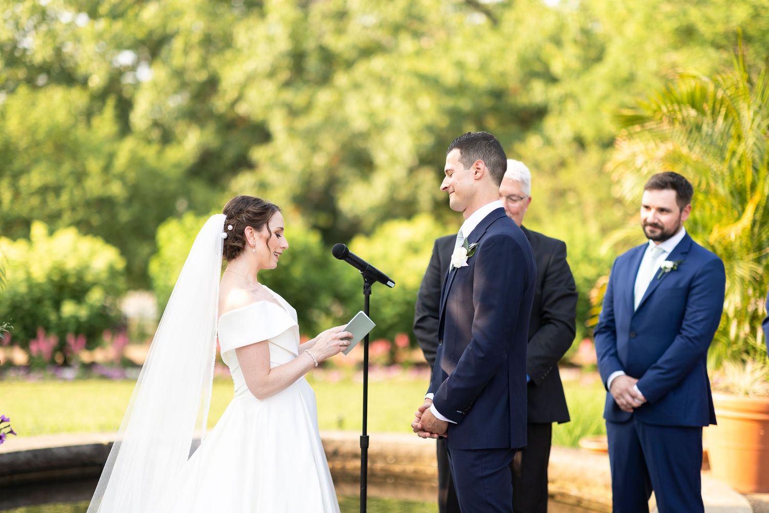 Couple exchanging vows during outdoor garden wedding ceremony with palm trees in background.