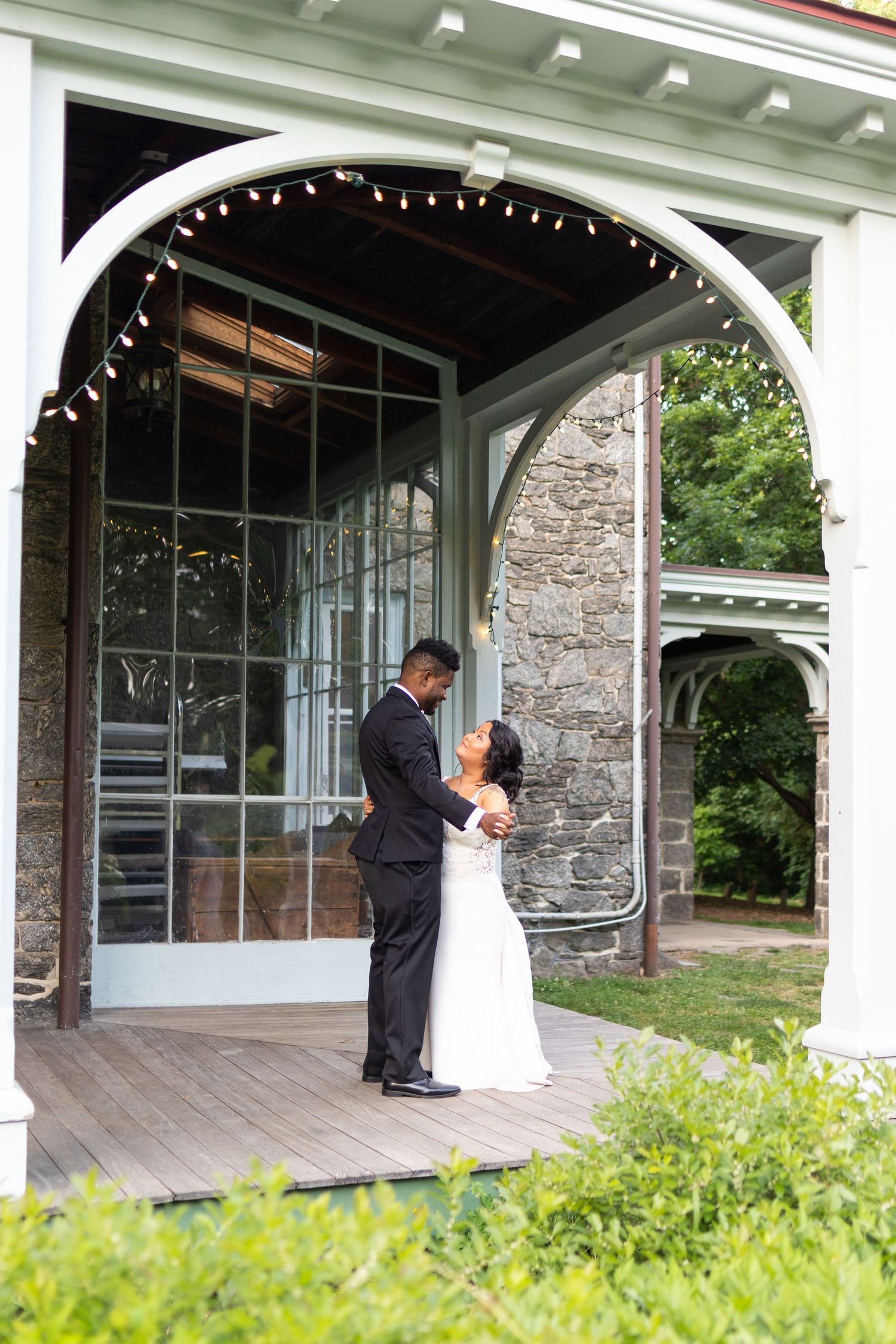 Wedding couple shares intimate moments on a stone building's covered veranda with white columns.