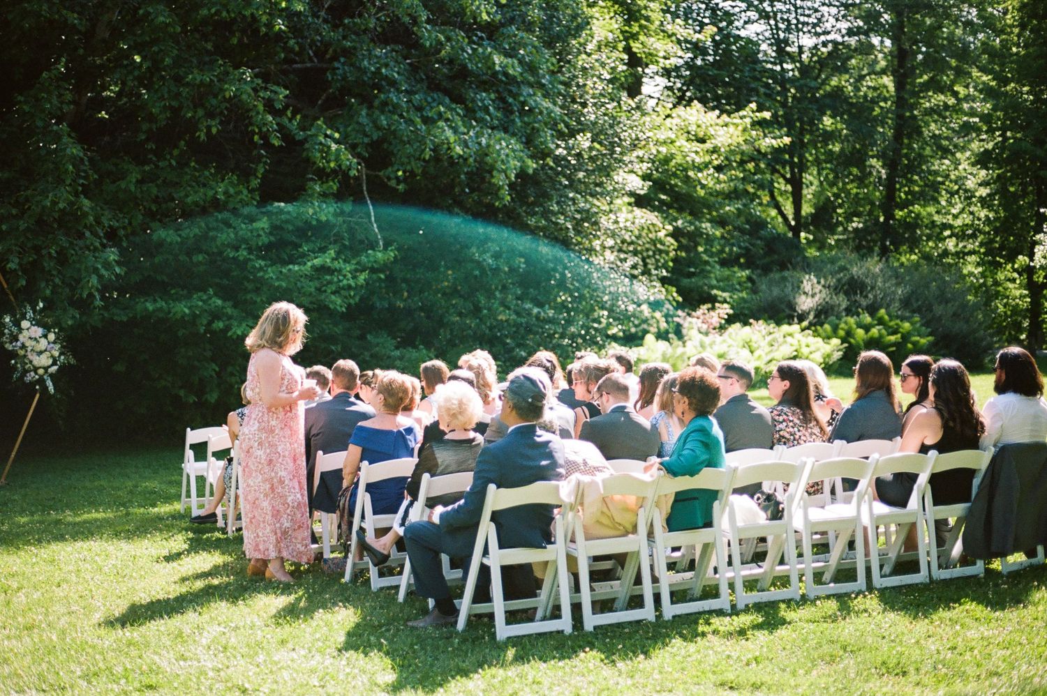 Outdoor wedding ceremony setup with white chairs arranged in rows under shady trees.