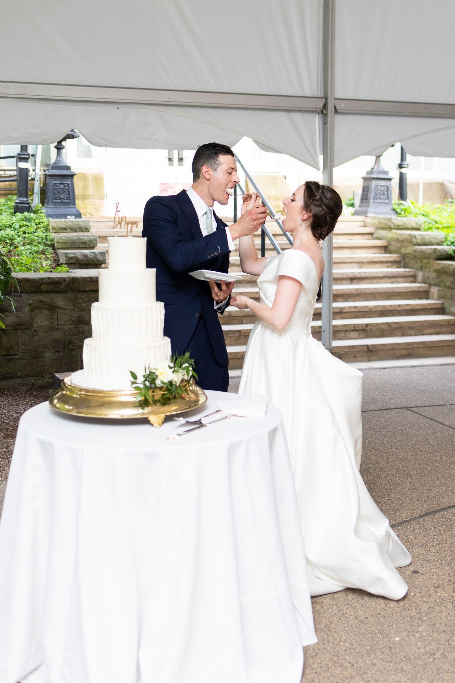 Newlyweds share cake feeding moment beside their elegant white wedding cake.