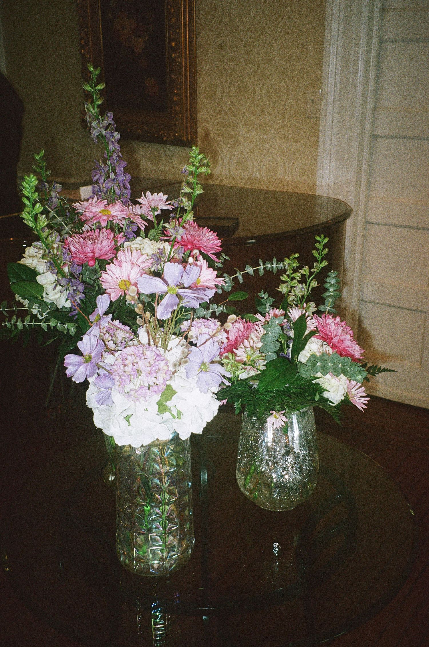 Pink and purple floral arrangements in glass vases displayed on a dark table.
