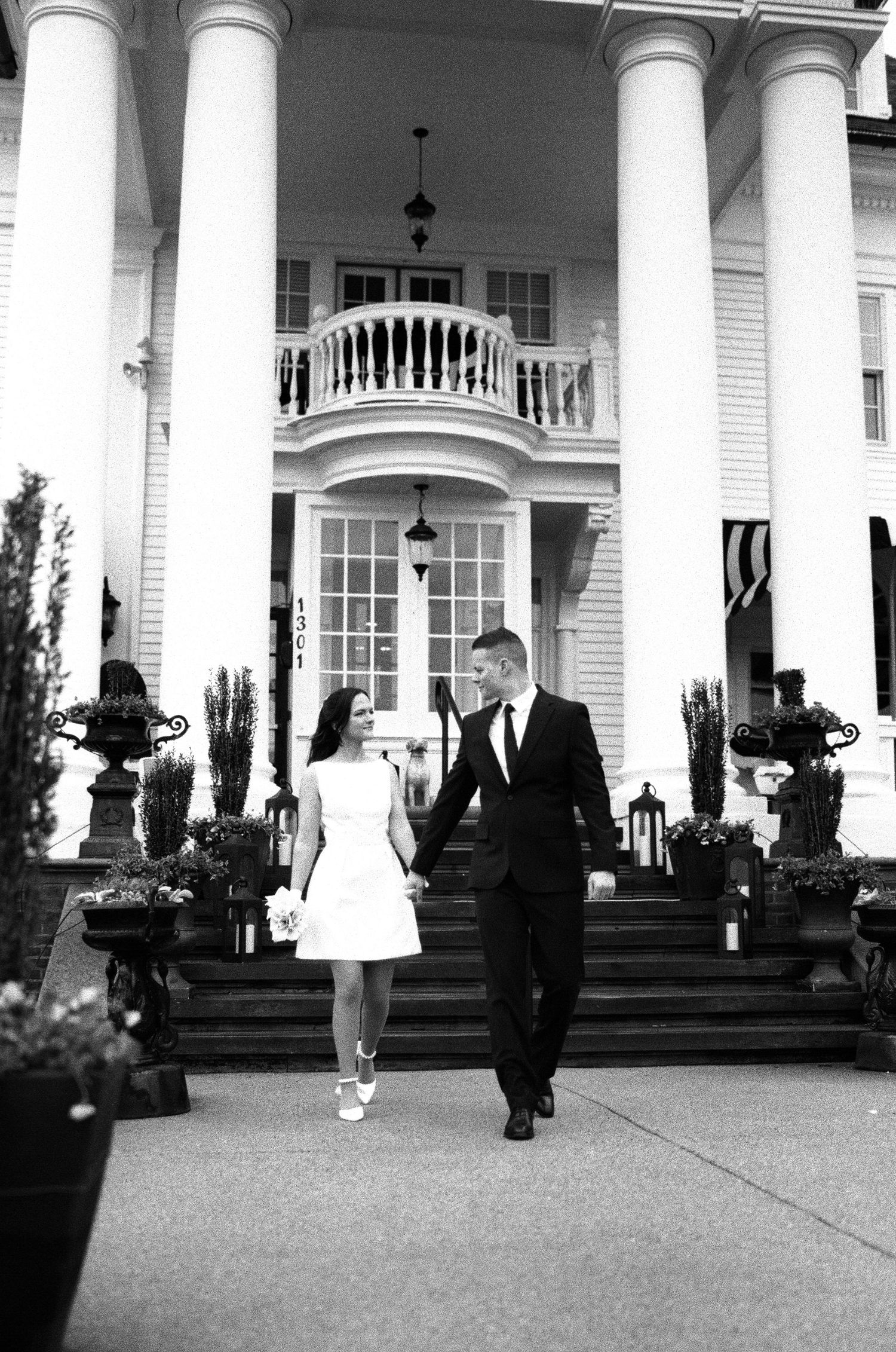 Black and white photo of wedding party on grand columned porch of historic mansion.