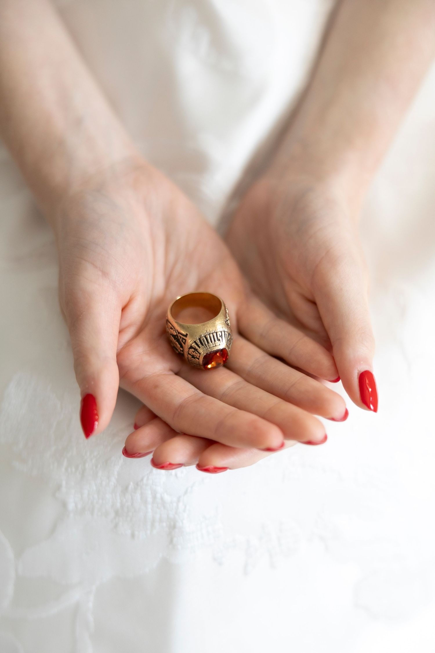 Close up of manicured hands holding vintage ring against white fabric.