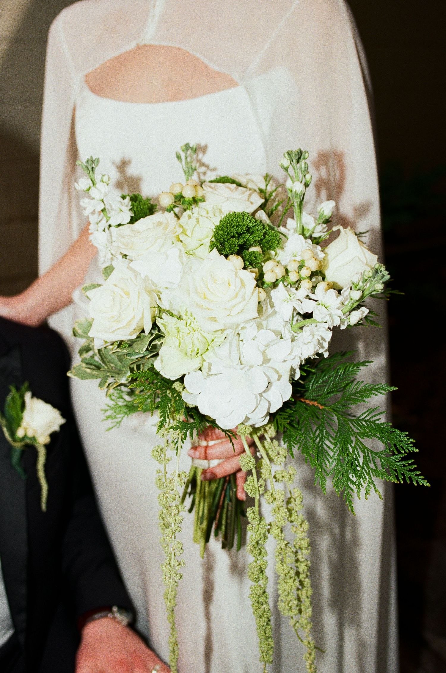 Bride holding elegant white and green wedding bouquet with roses, hydrangeas, and trailing greenery.