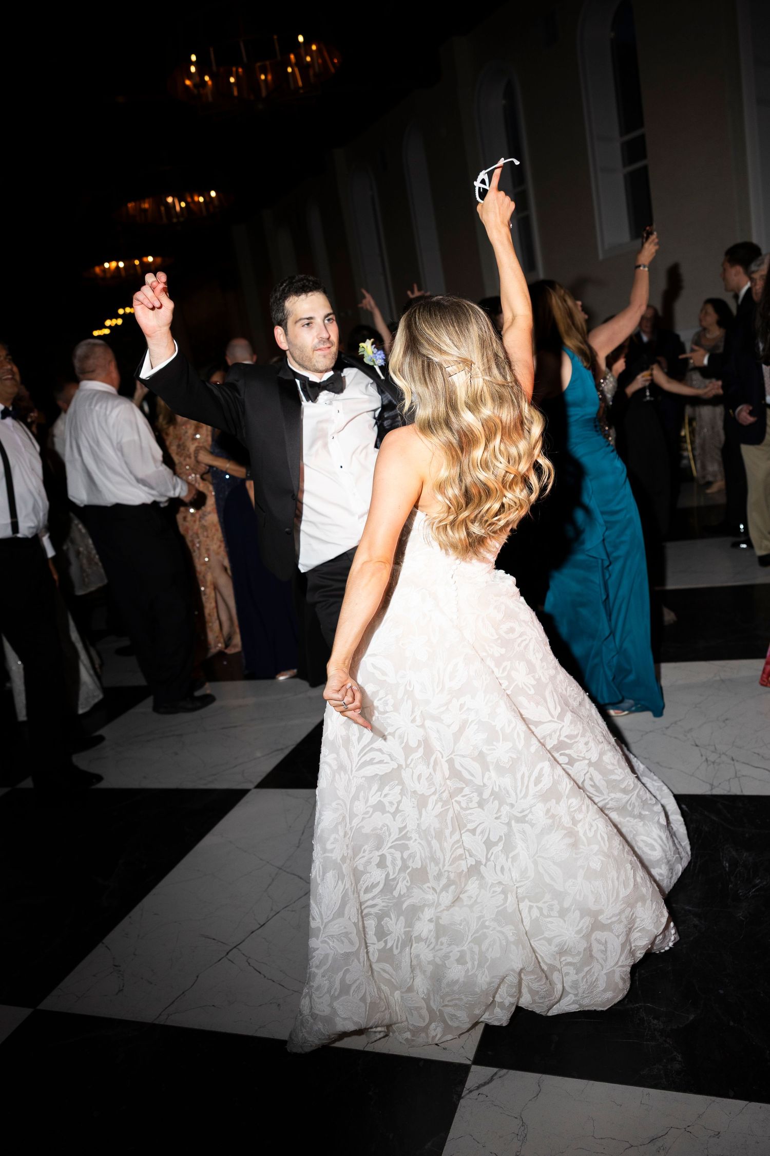 Wedding guests dancing on a dark dance floor with a bride in a flowing white dress.