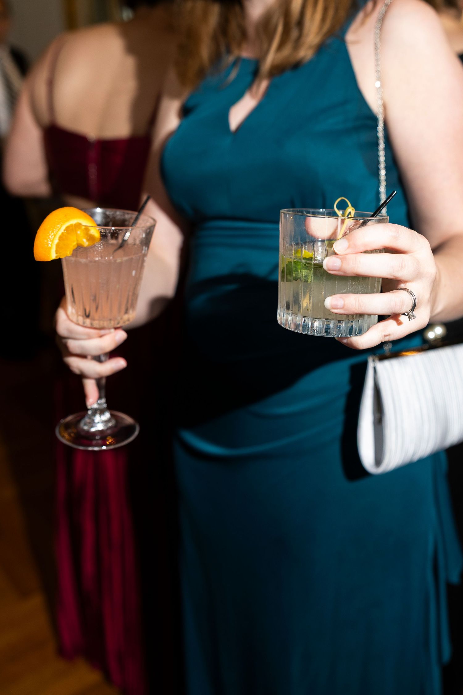 Wedding guests in teal dresses holding cocktail glasses garnished with citrus.