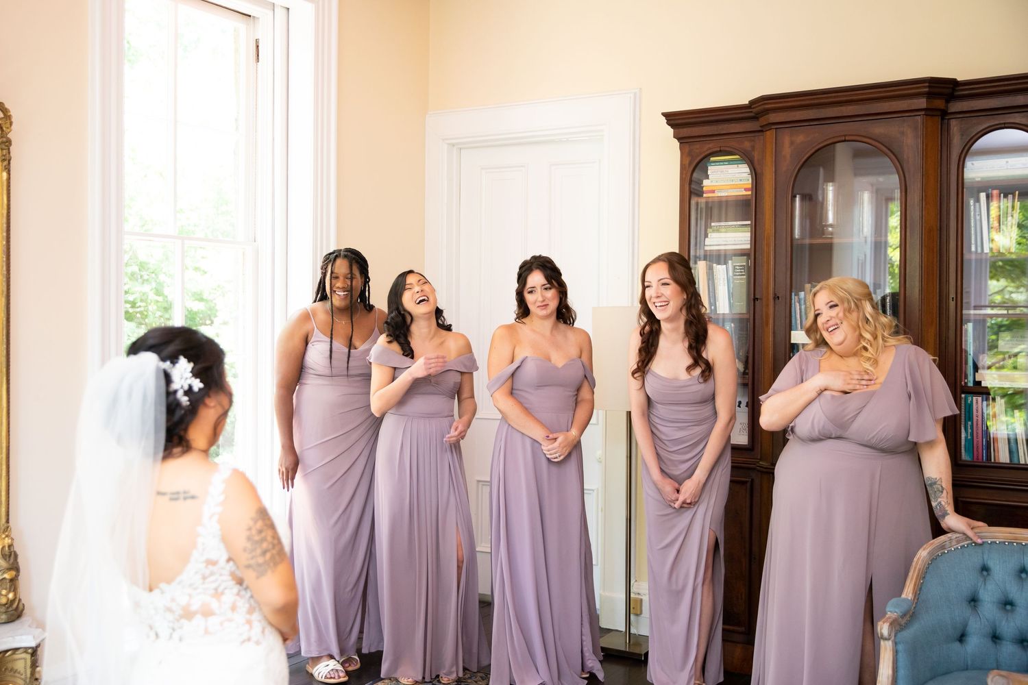 Bridesmaids in matching lavender dresses line up for wedding photos in an elegant room.