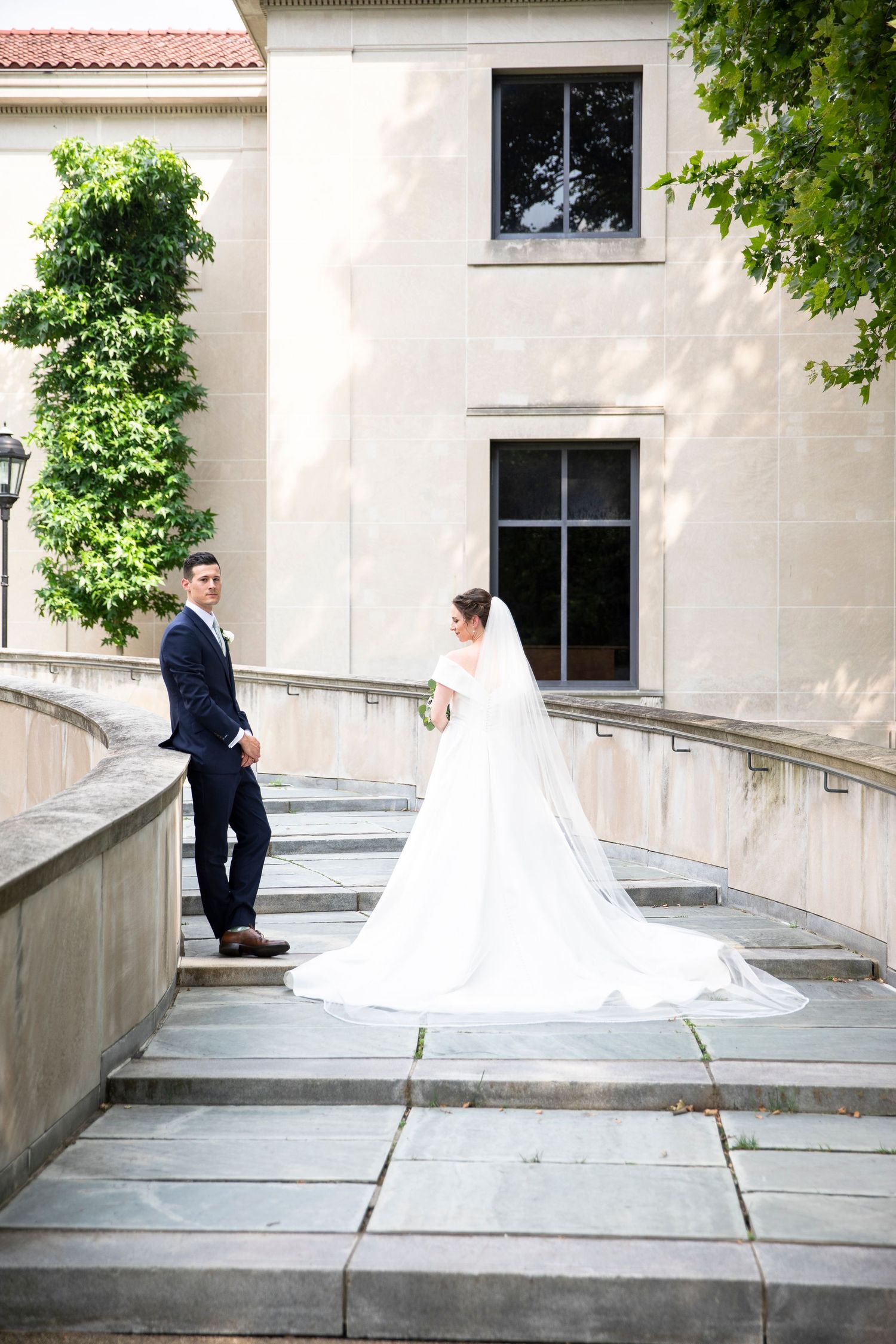 Wedding couple shares a moment on curved stone steps against white building facade.