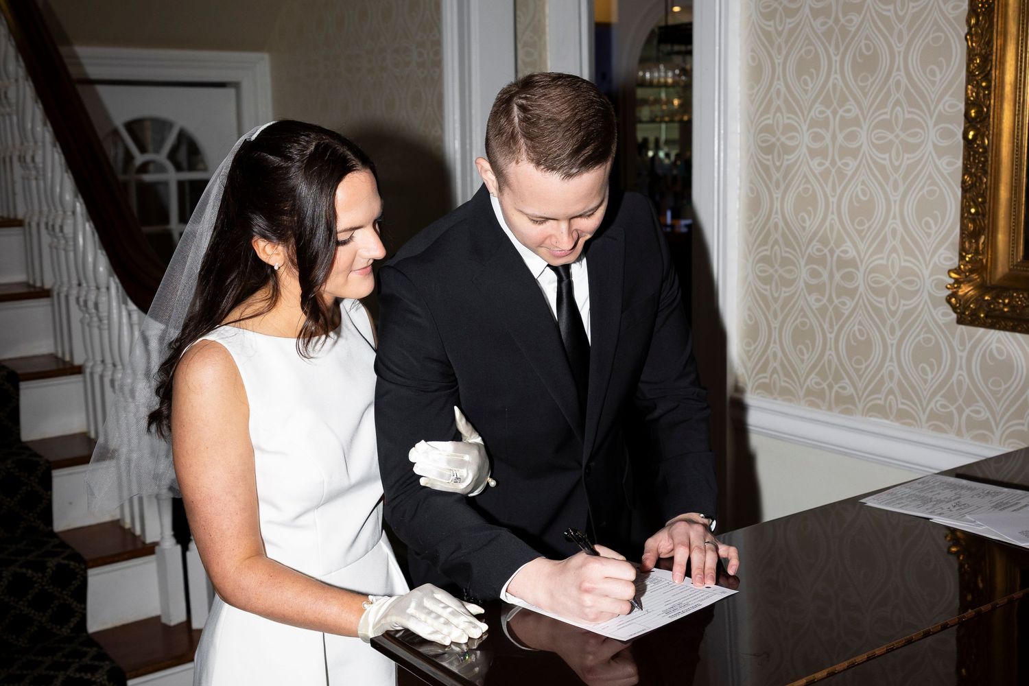 Couple signing documents in formal attire at an indoor venue.