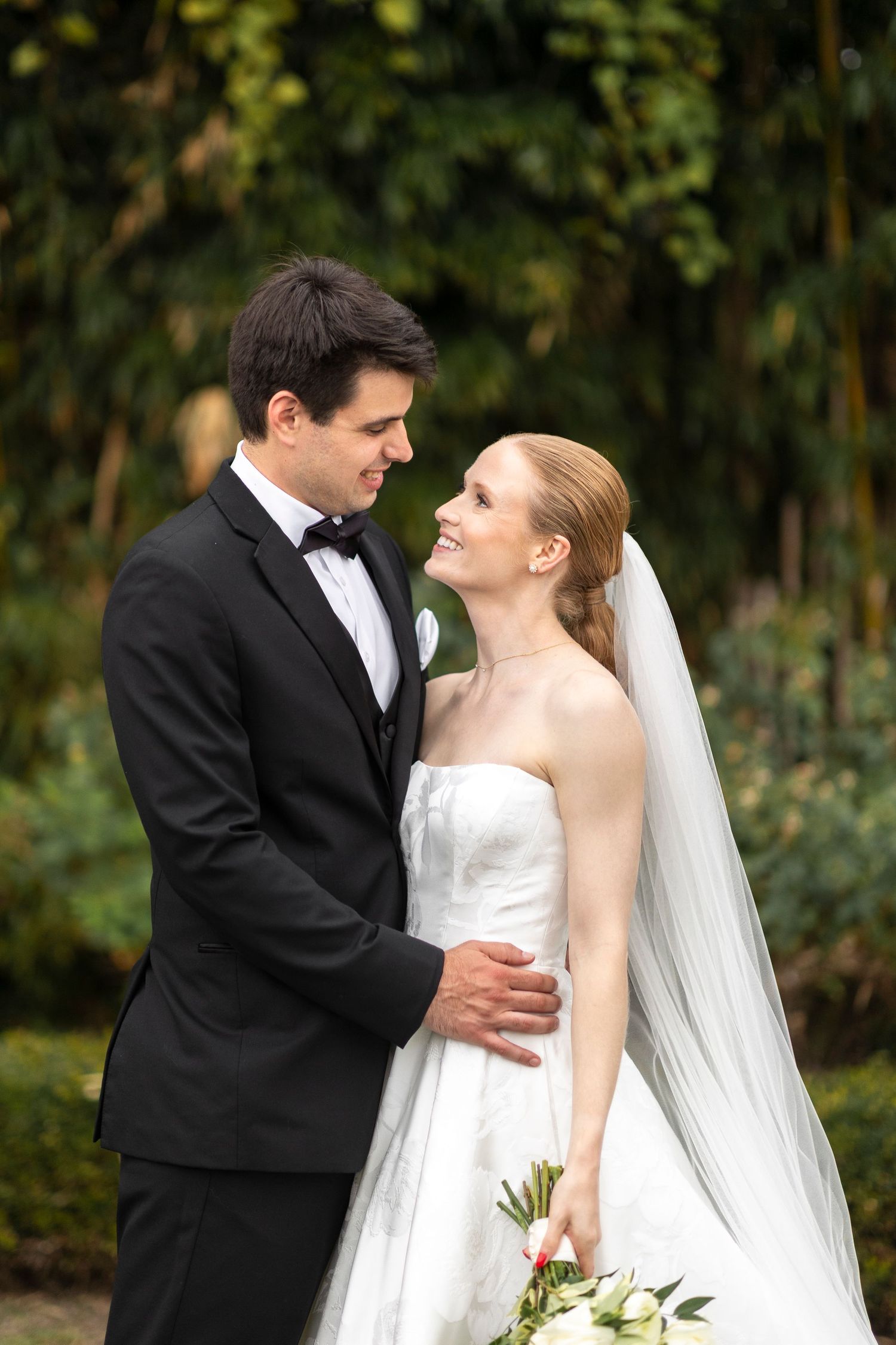 A tender wedding moment between a couple in formal attire against a garden backdrop.