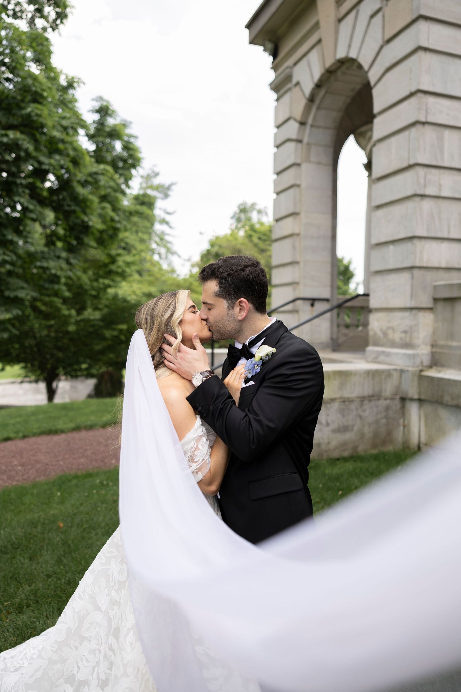 Romantic wedding moment captured with flowing veil against stone architecture backdrop.