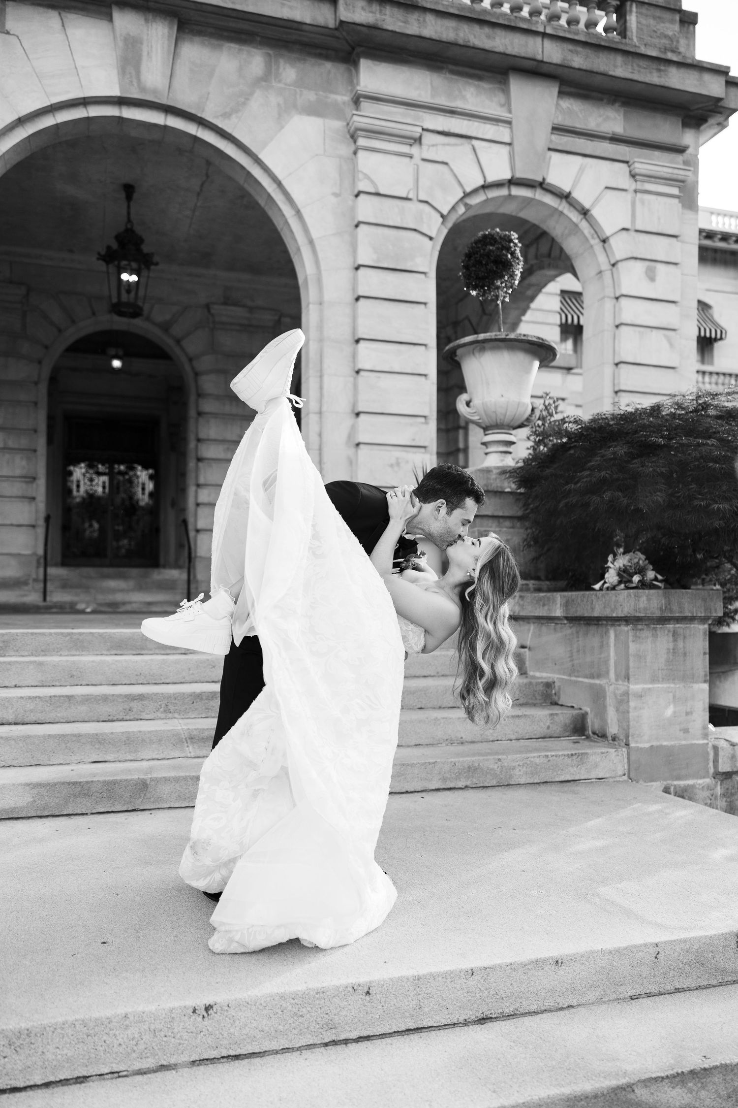 A sequence of black and white photos showing a couple in wedding attire on stone steps of a historic building.
