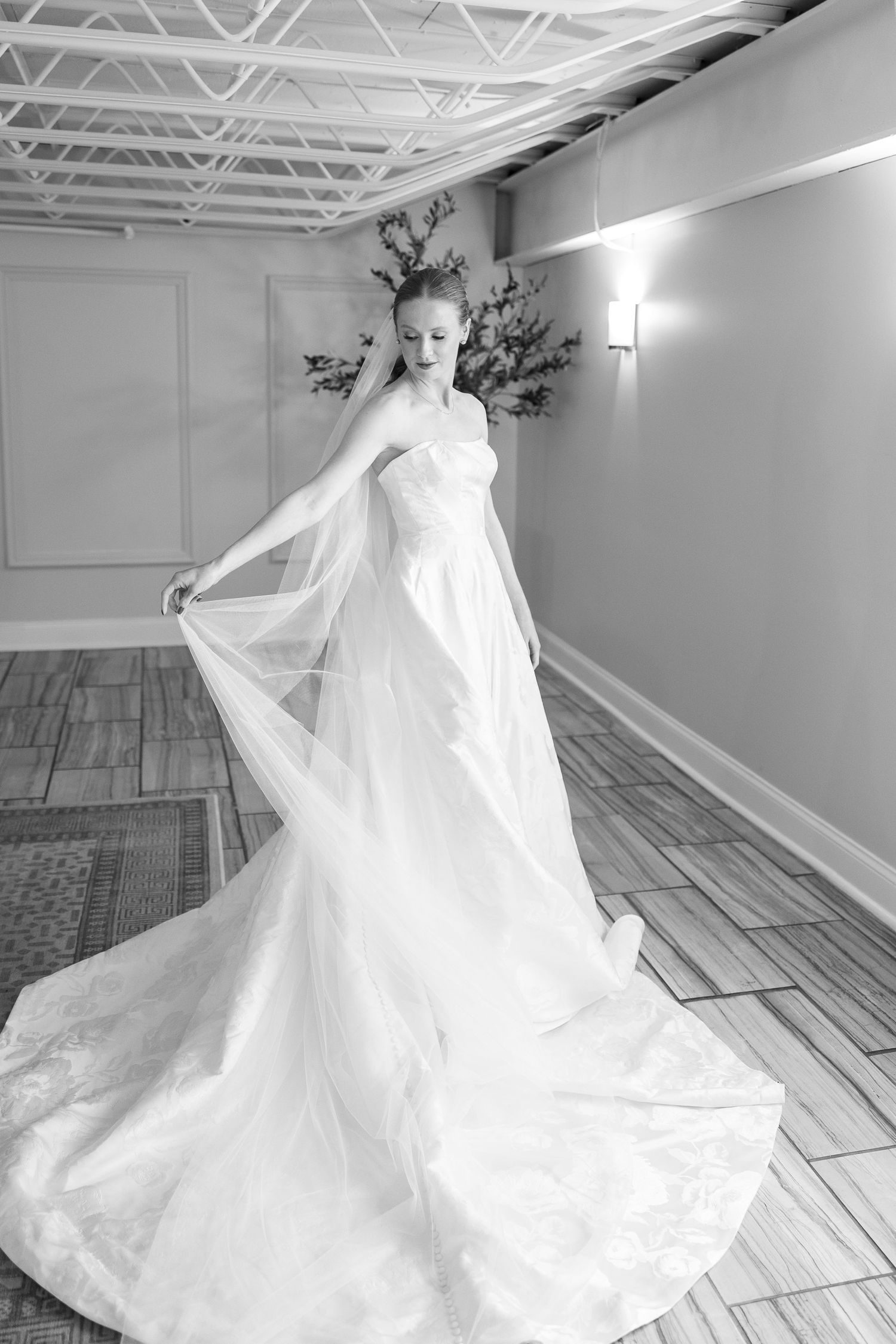 Wedding dress with dramatic train flows across light wooden floor in minimalist studio space.