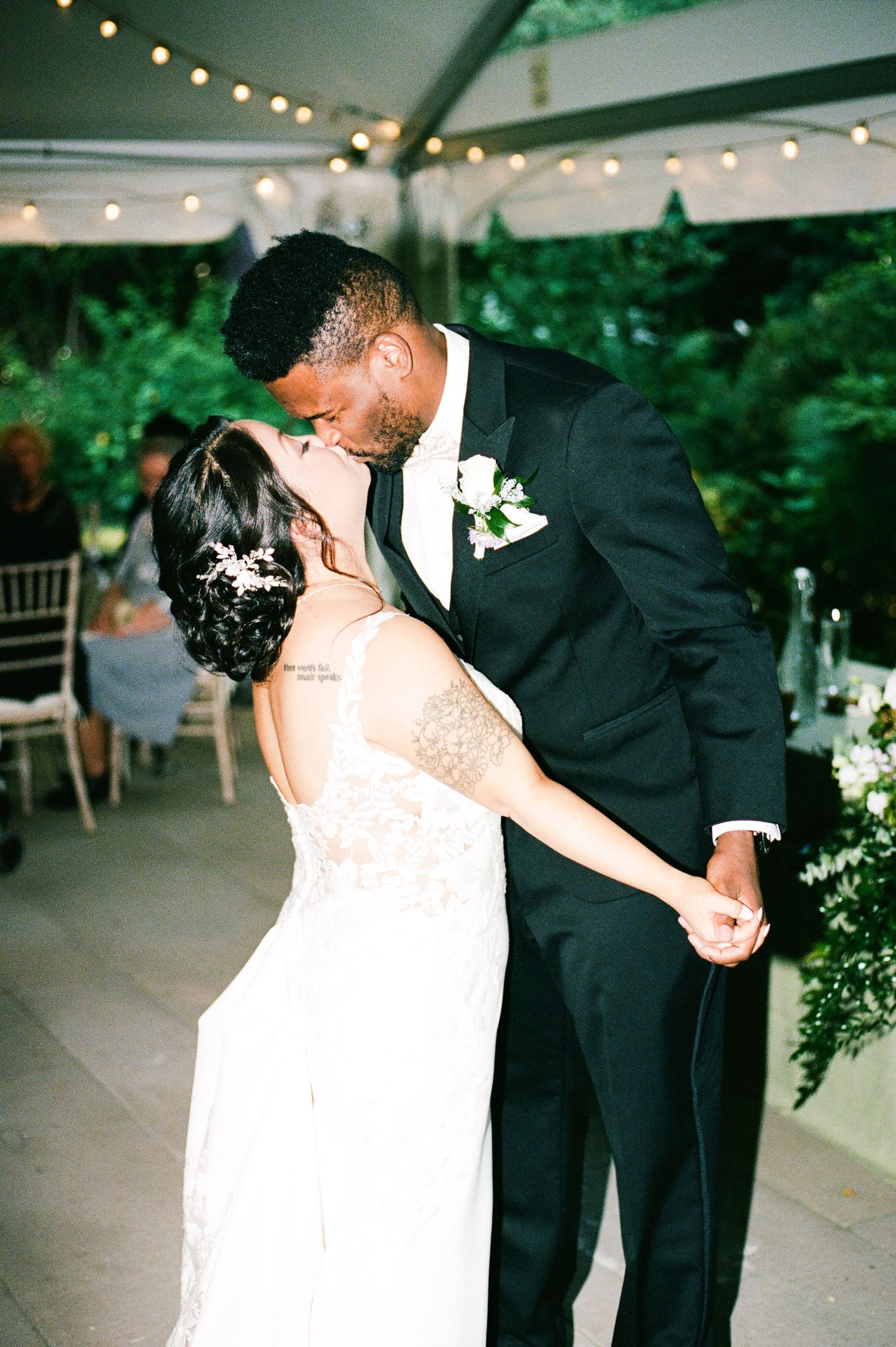 Romantic first dance under string lights at an outdoor wedding reception.