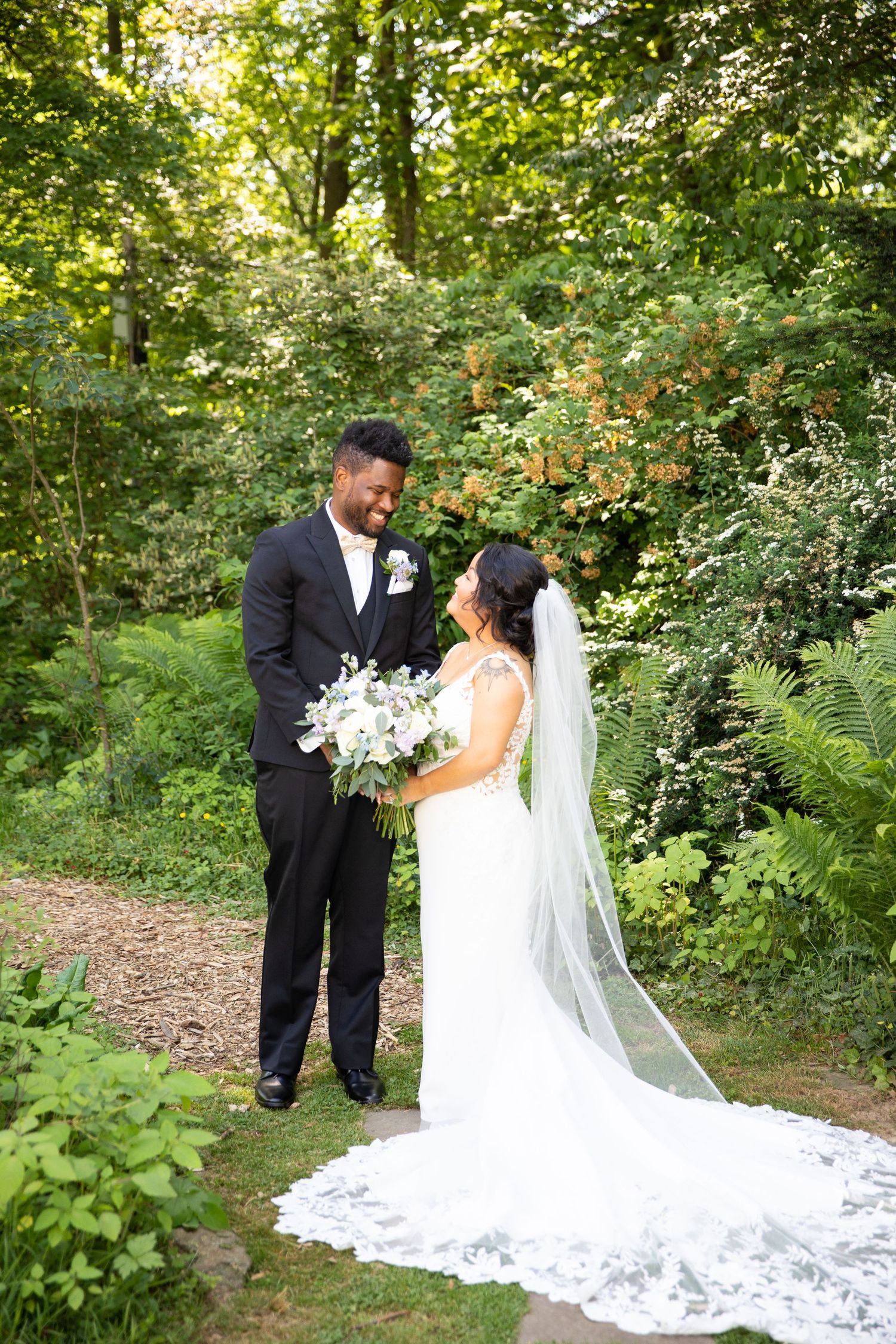 A couple shares an intimate moment on their wedding day surrounded by lush garden greenery.