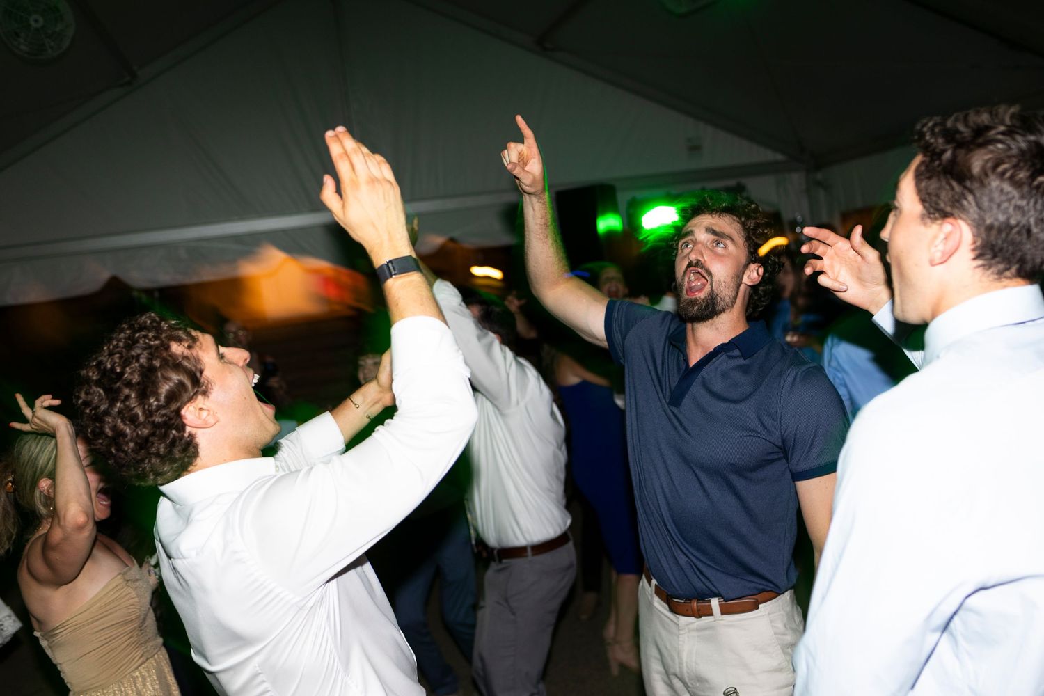 Energetic crowd dancing with hands in the air at an indoor wedding reception.