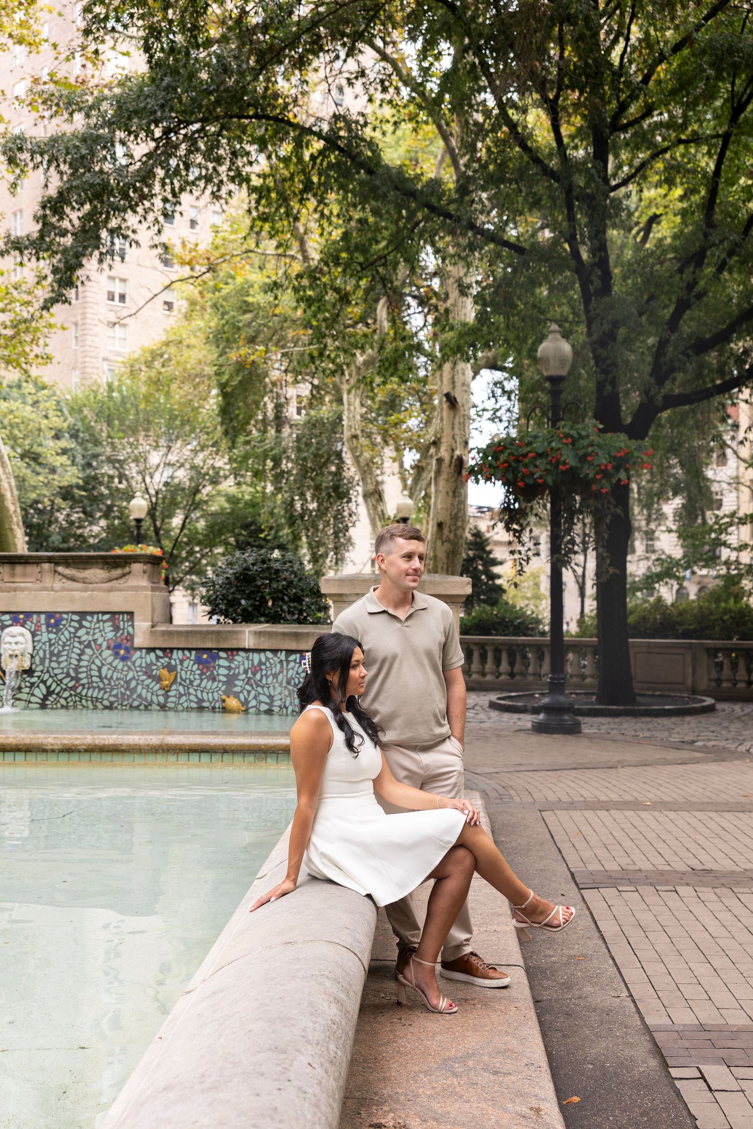 A couple sits together on a stone ledge in an urban park setting.