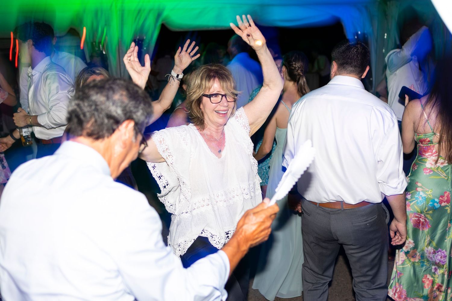 Dance floor filled with party guests under vibrant green and blue lighting effects.