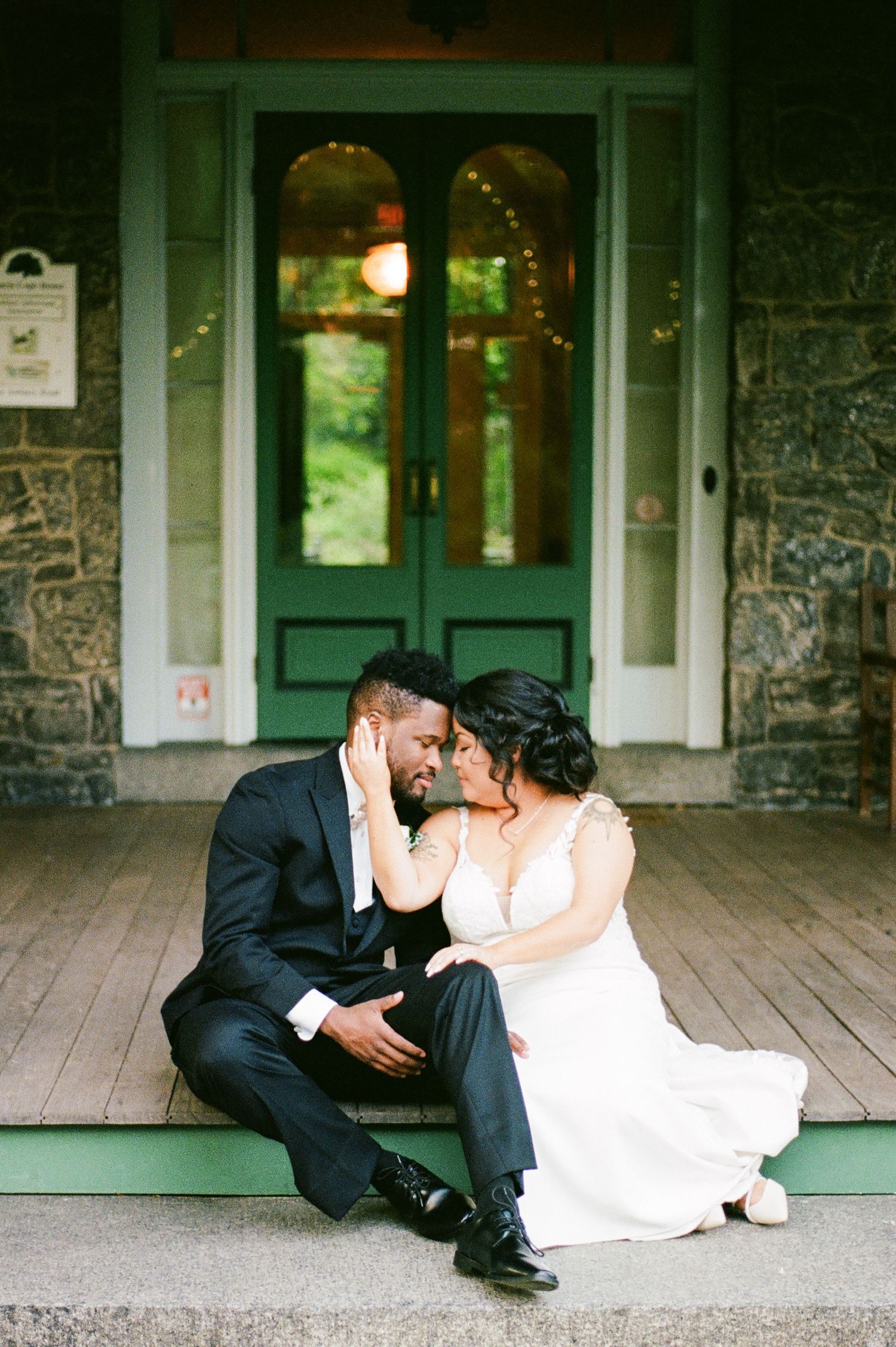 Wedding couple sitting playfully on rustic porch steps of stone building.