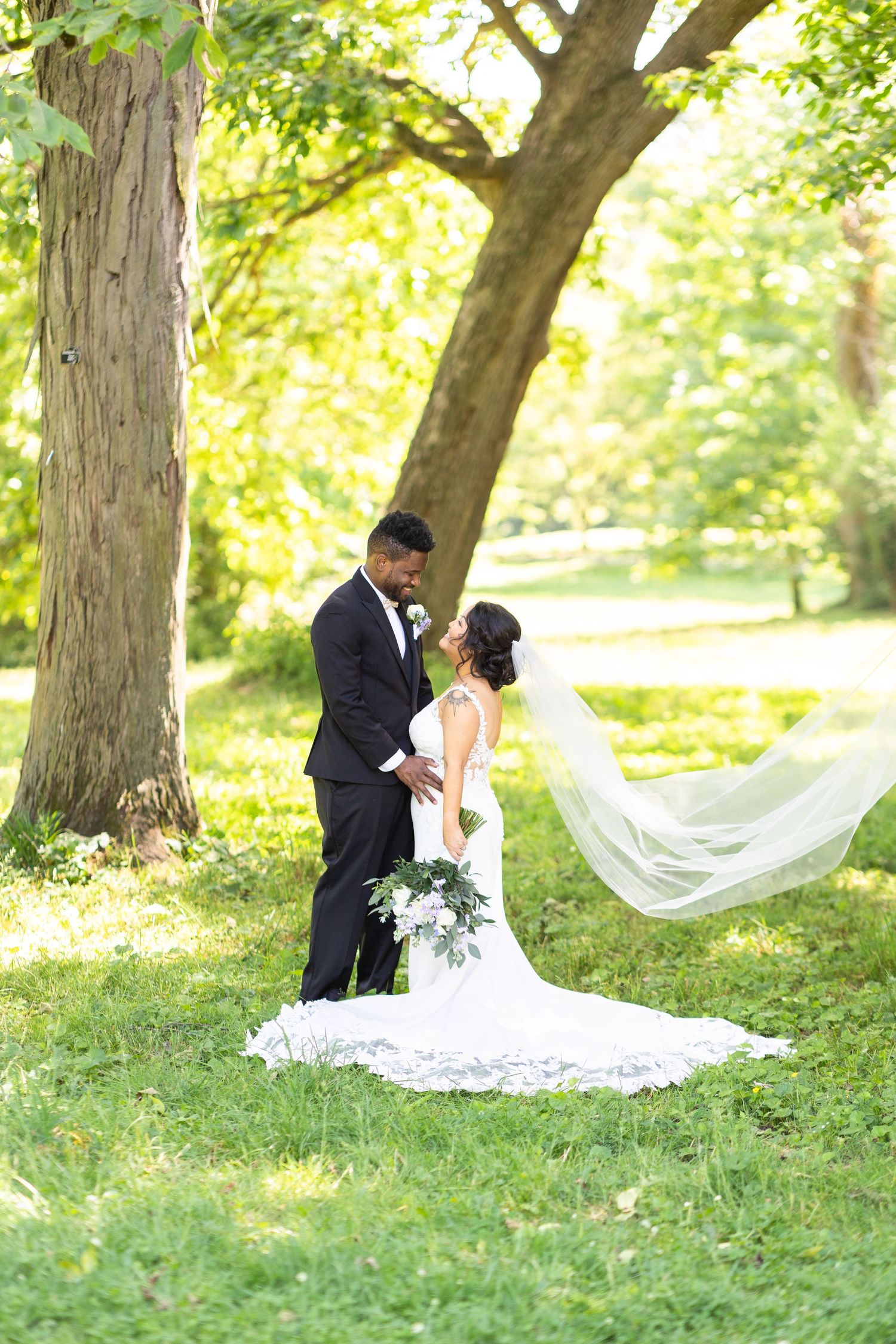 A romantic wedding portrait of a couple with a flowing veil in a sunlit park.
