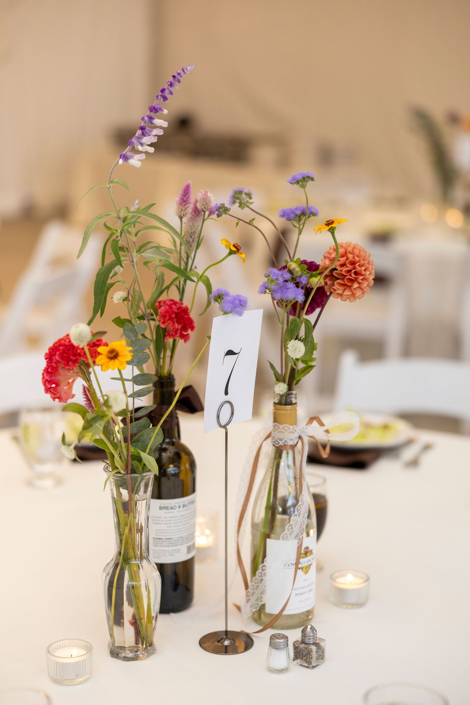 Wedding reception table decorated with colorful wildflowers in glass vases and table numbers.