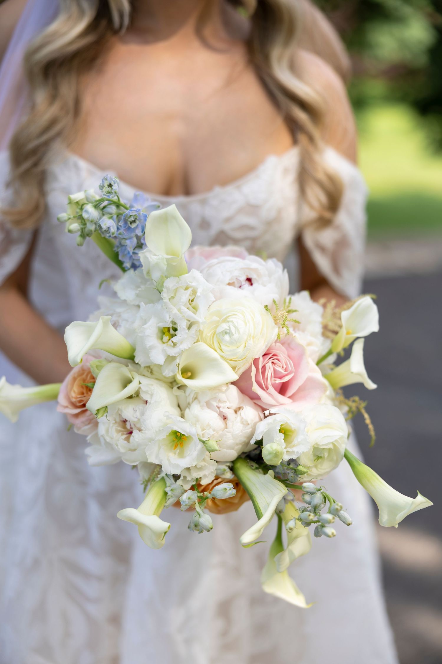 Elegant bridal bouquet featuring white lilies, pink roses and delicate blue flowers against a white dress.