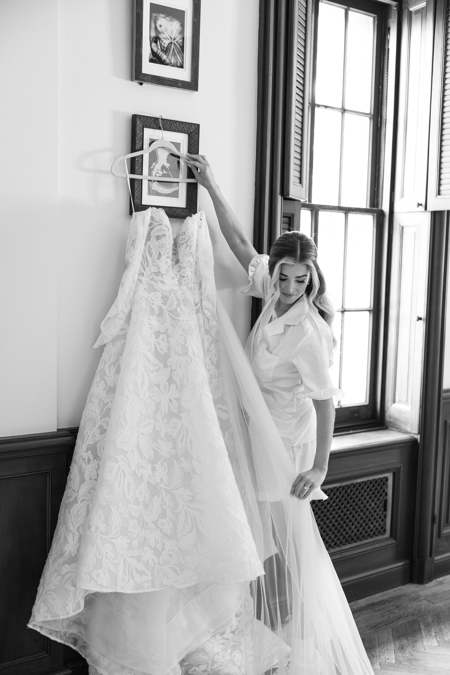 Multiple white wedding dresses hanging on display in a room with dark trim windows.
