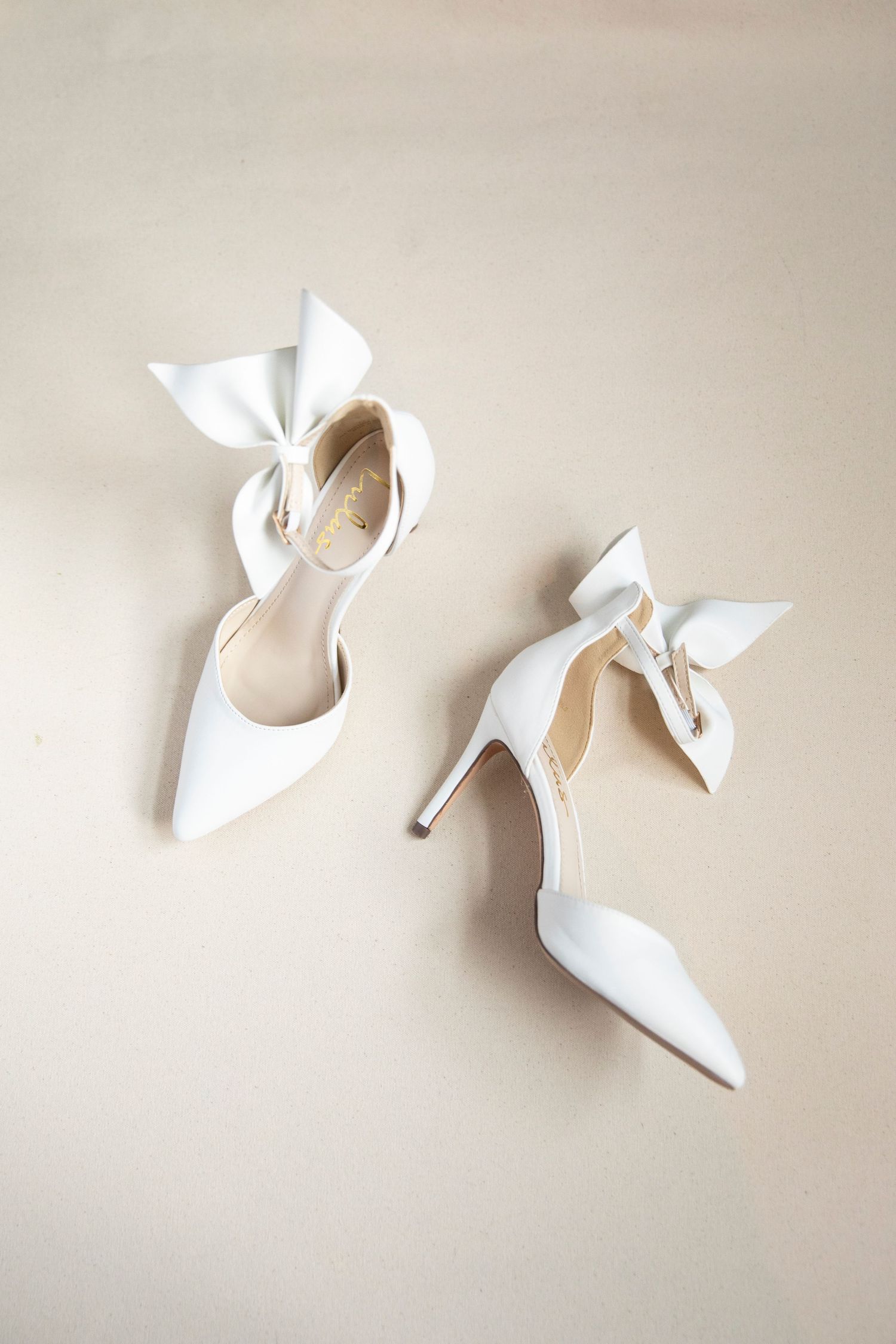 Elegant white bridal shoes with bow details displayed on a neutral background.