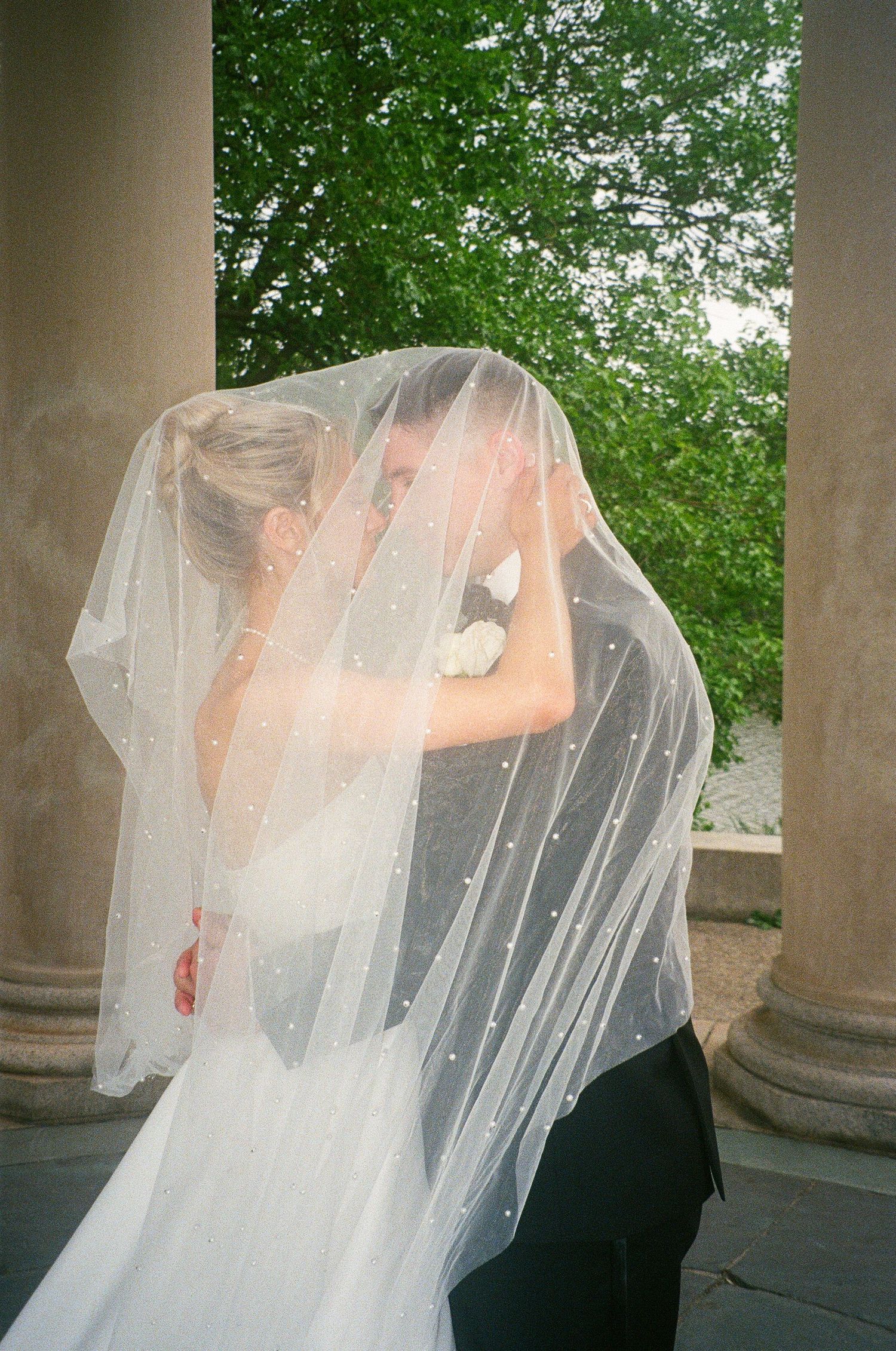 Romantic moment captured under a veil in an outdoor setting with green foliage.