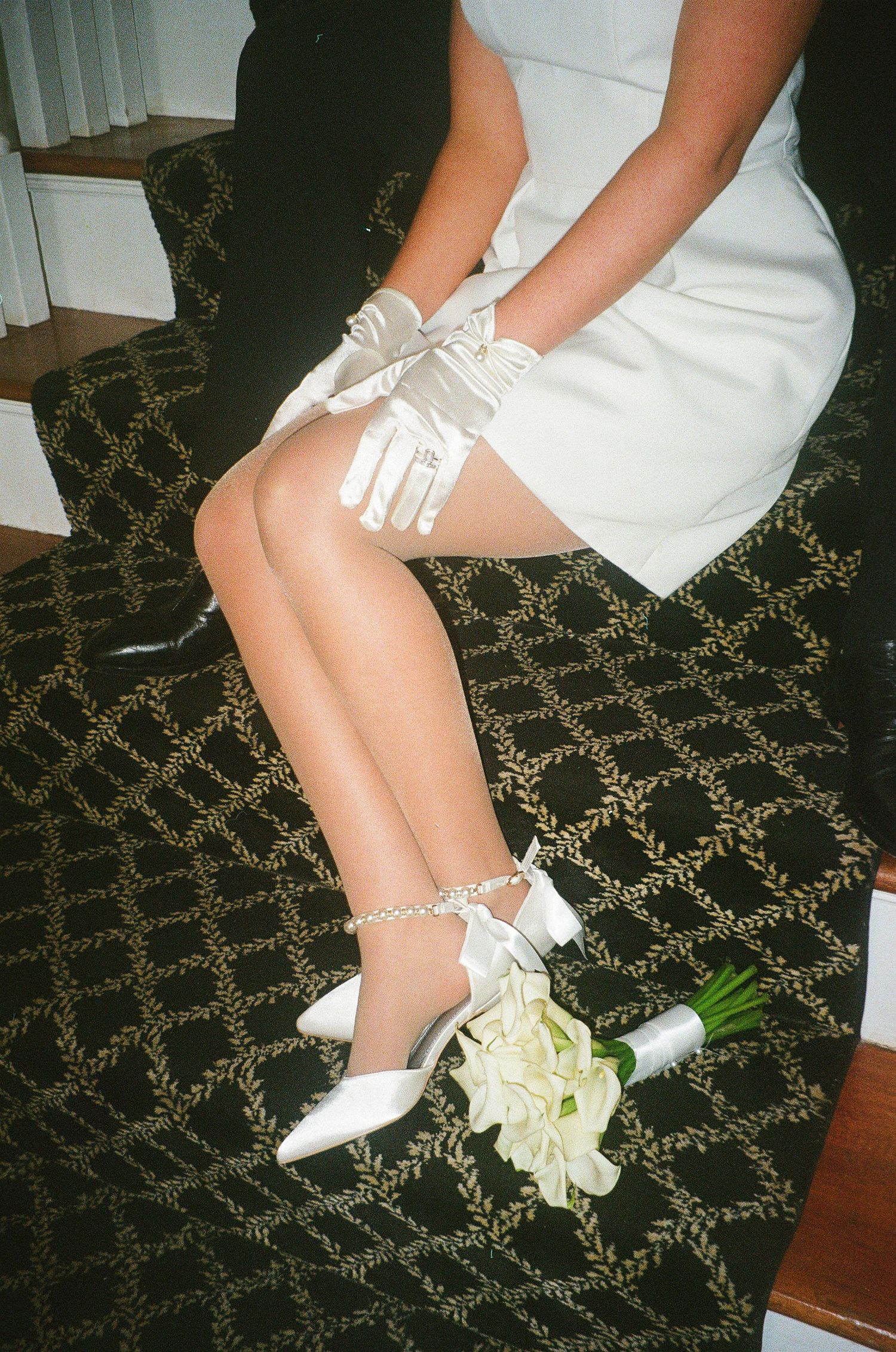 White bridal shoes and bouquet on patterned carpet floor.