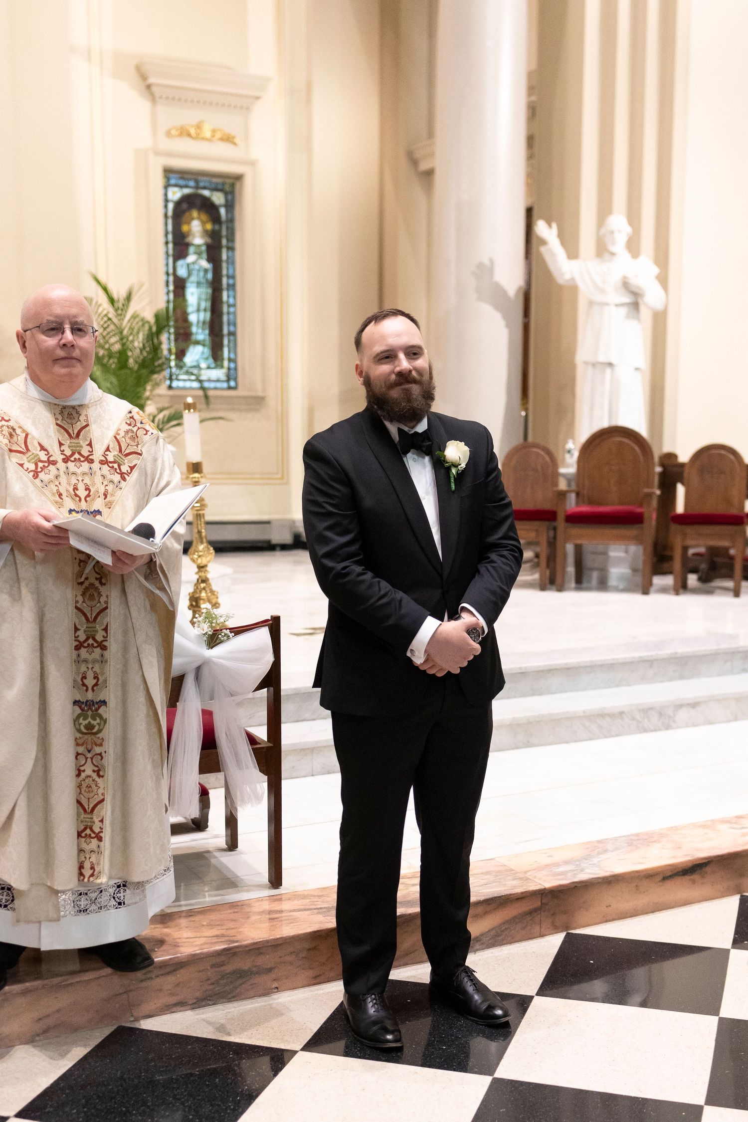 Clergy member and groomsman standing at church altar during wedding ceremony.