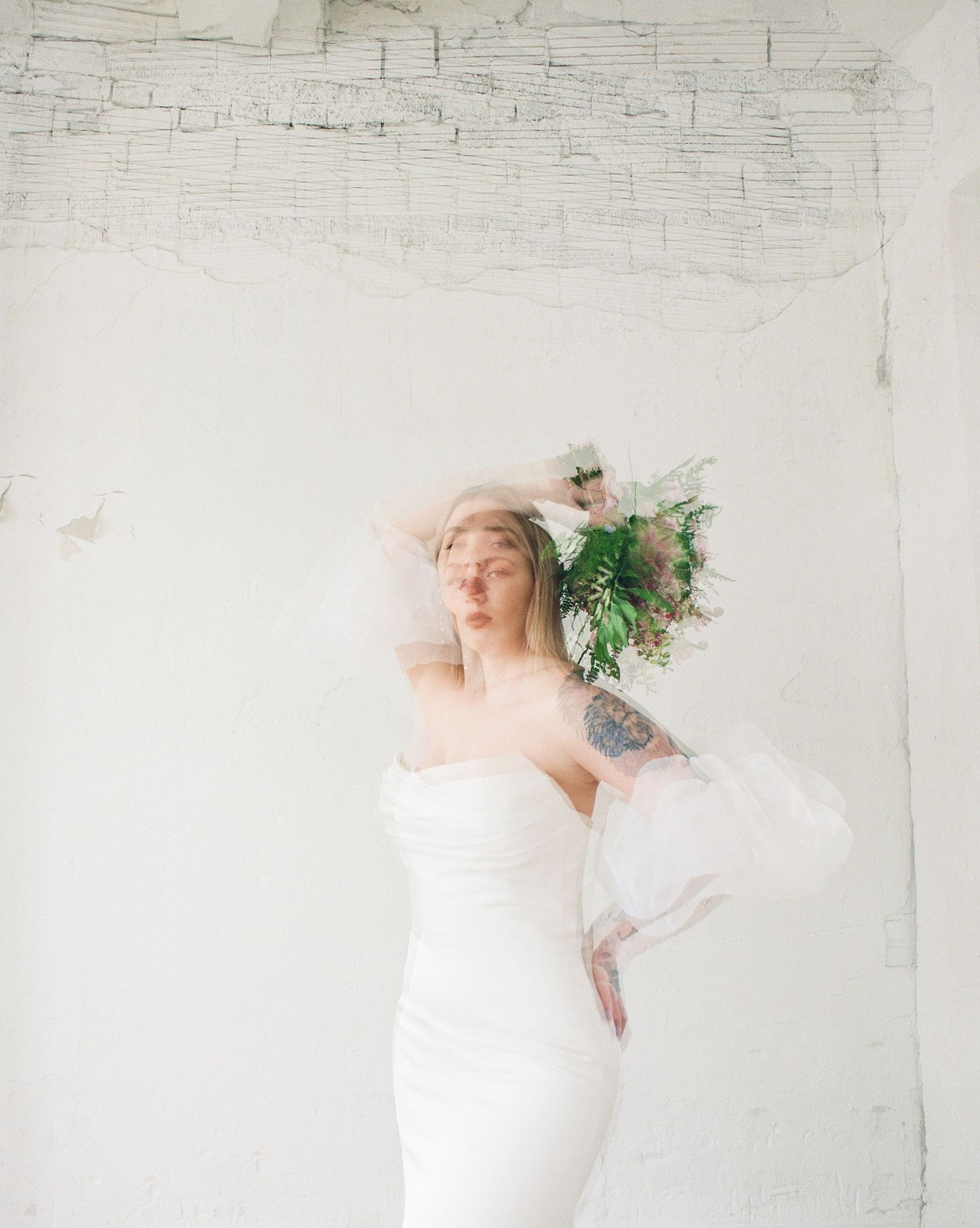 Artistic bridal portrait with motion blur and floral elements against white brick wall.