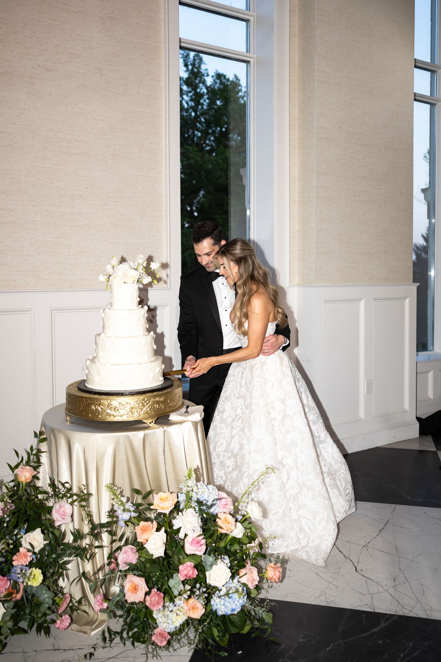 Wedding cake cutting ceremony in an elegant white room with floral decorations.