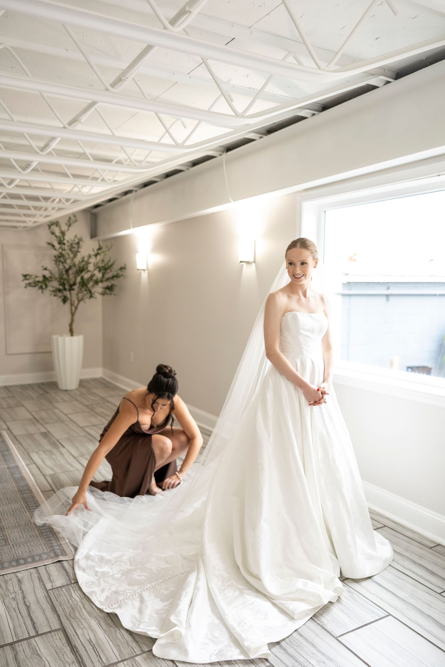 Wedding dress preparation scene with elegant white gown and flowing train in modern minimalist space.