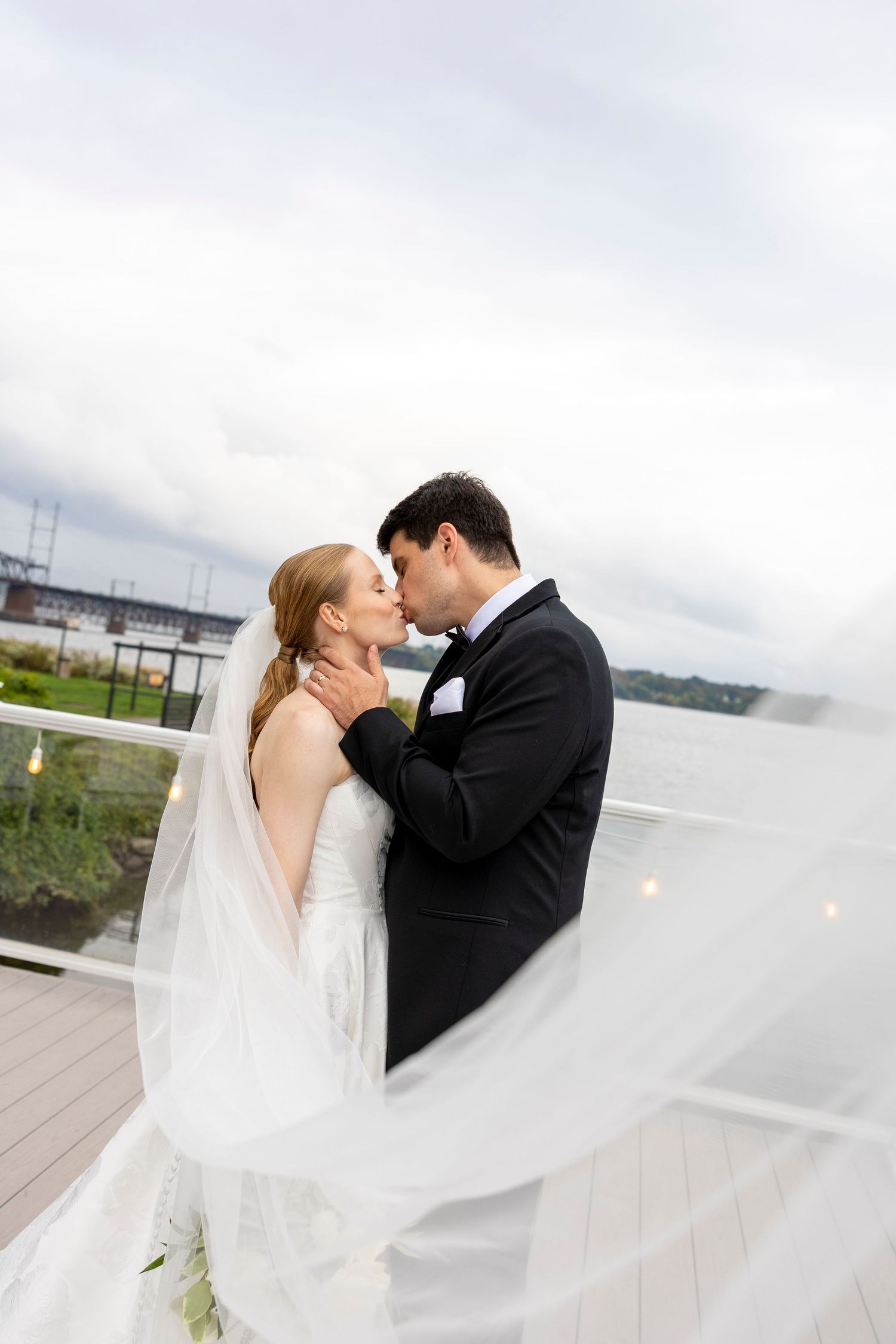 An intimate wedding portrait with a flowing veil against a waterfront backdrop.