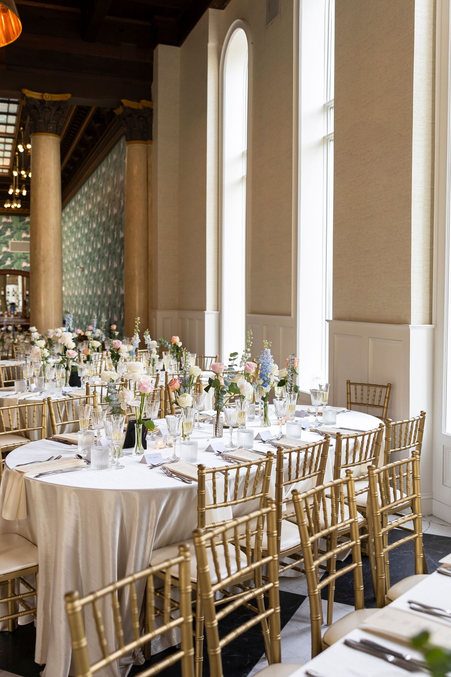 Wedding reception venue with gold chiavari chairs and round tables set with white linens.