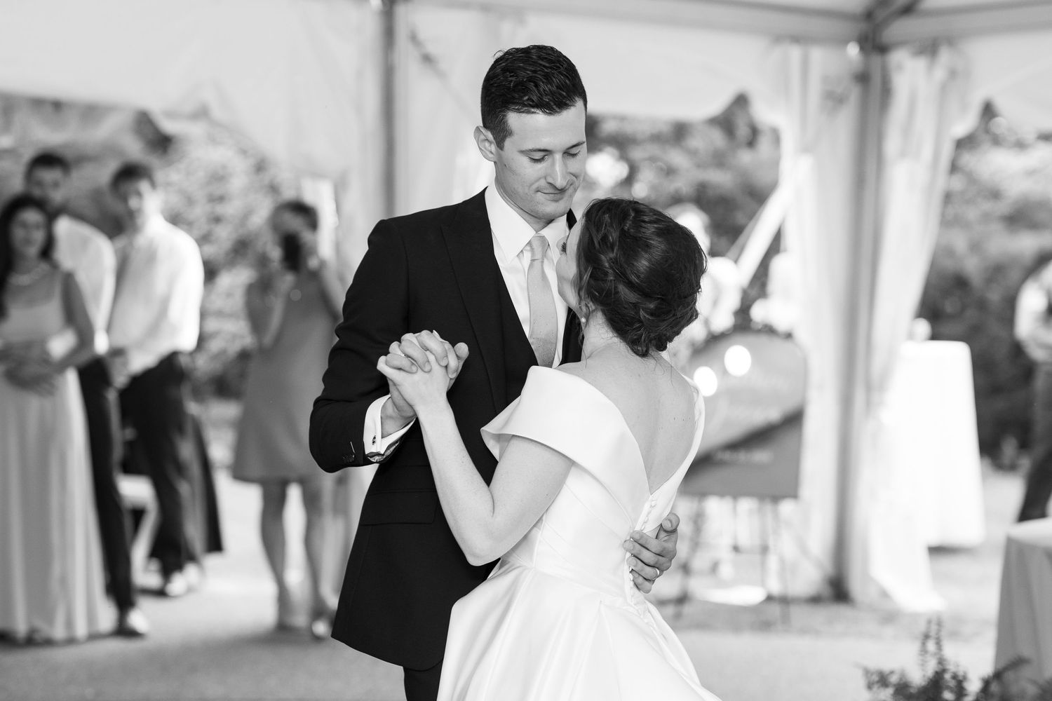 A romantic first dance between newlyweds under a white tent at their wedding reception.