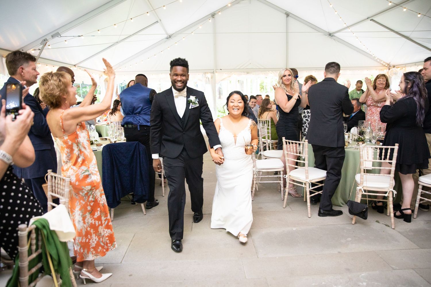 Wedding reception guests celebrate under a white tent with elegant decor.