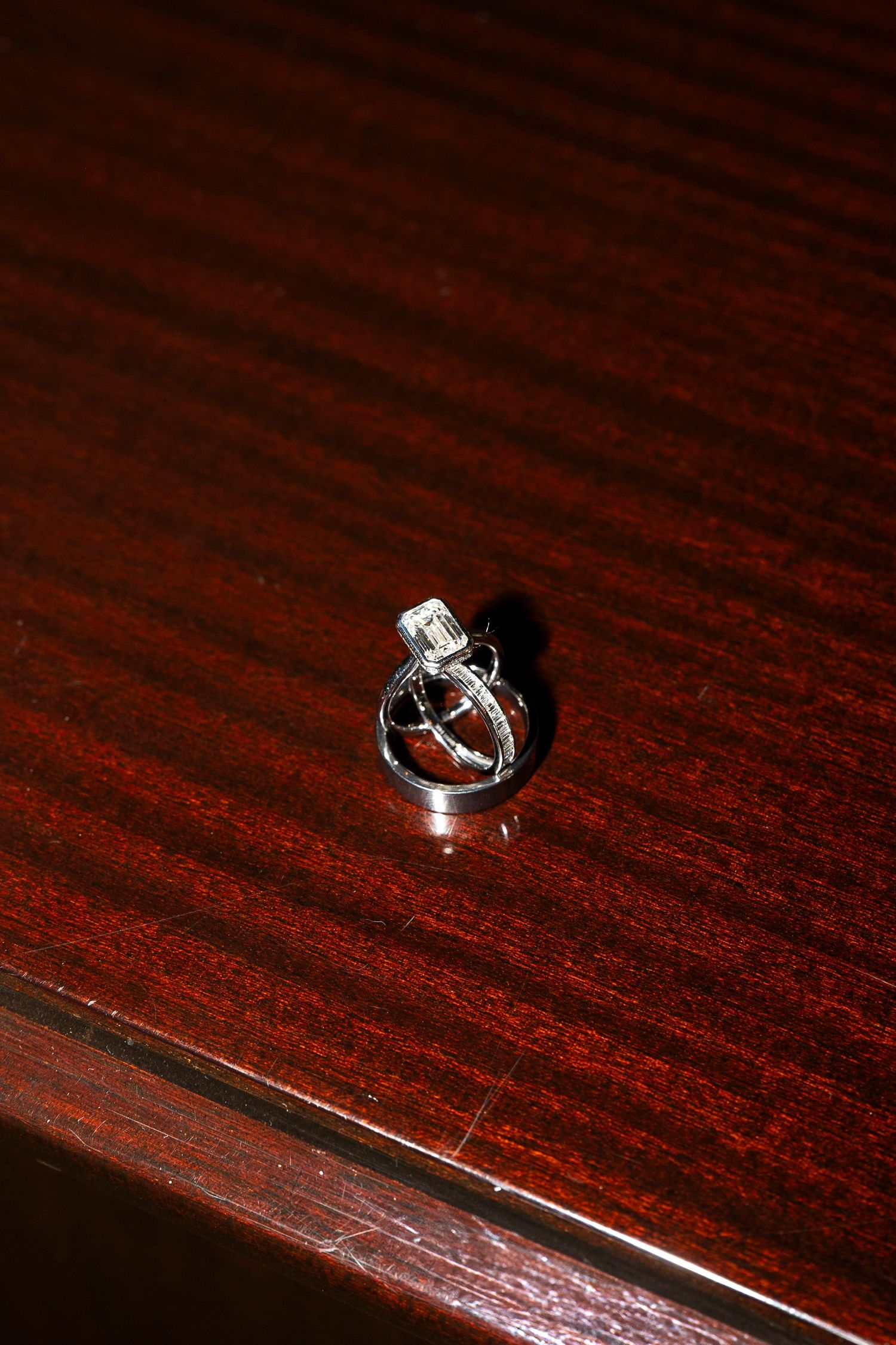 Wedding rings photographed on a dark wooden surface with dramatic lighting.