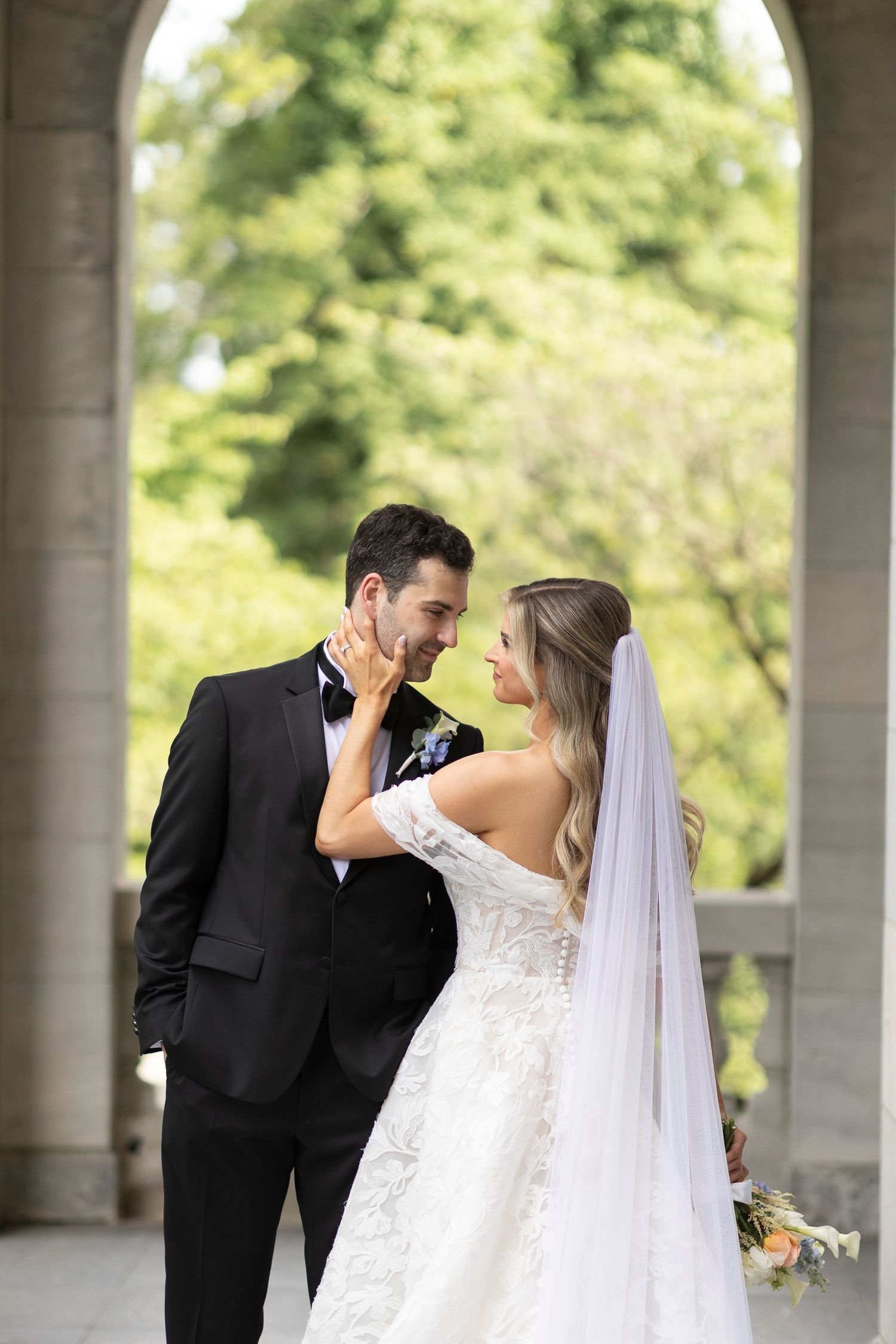 Romantic wedding portrait captured under a columned walkway surrounded by lush greenery.