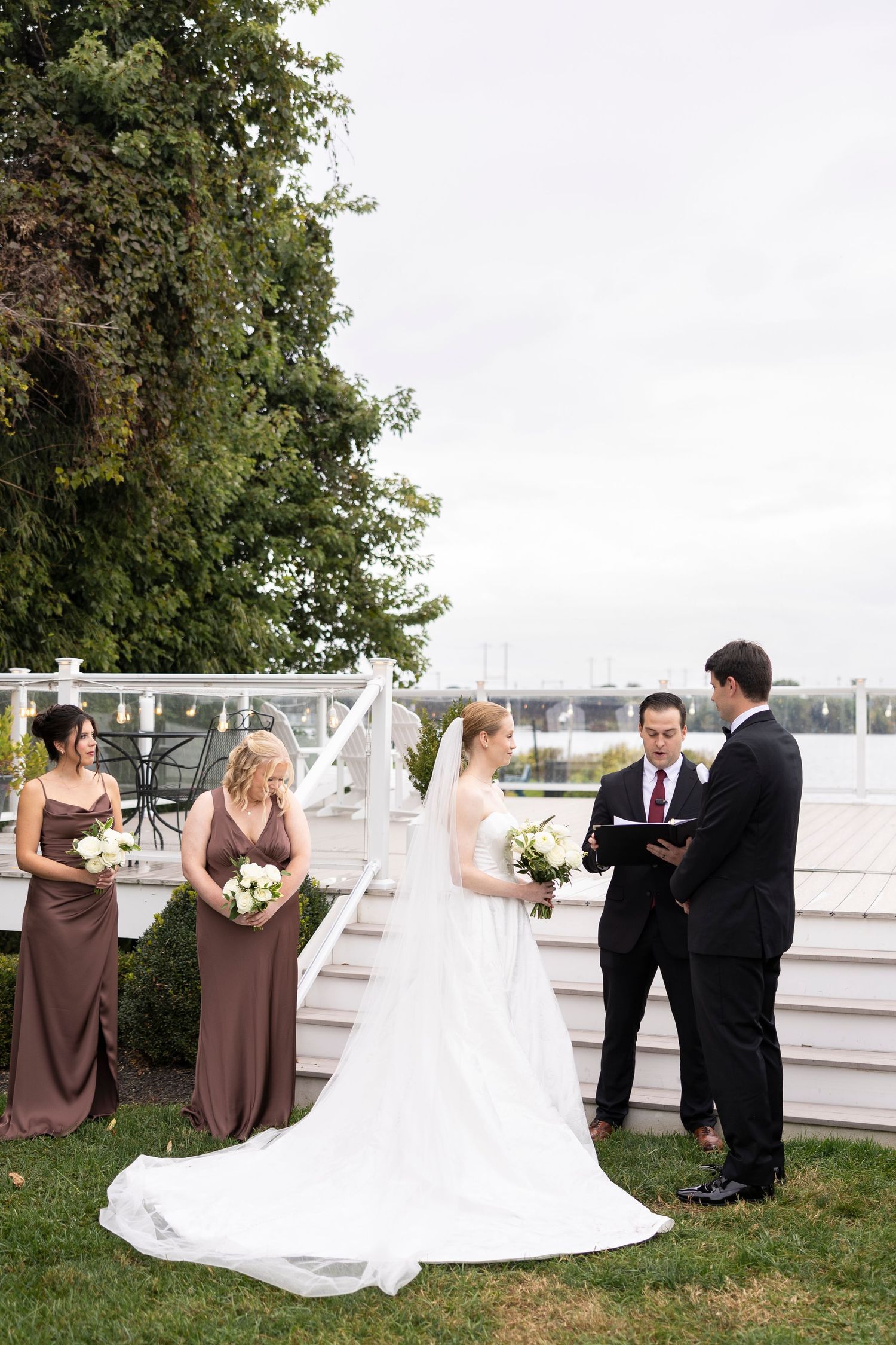 Wedding ceremony taking place outdoors with bridesmaids in brown dresses and a flowing white wedding gown.
