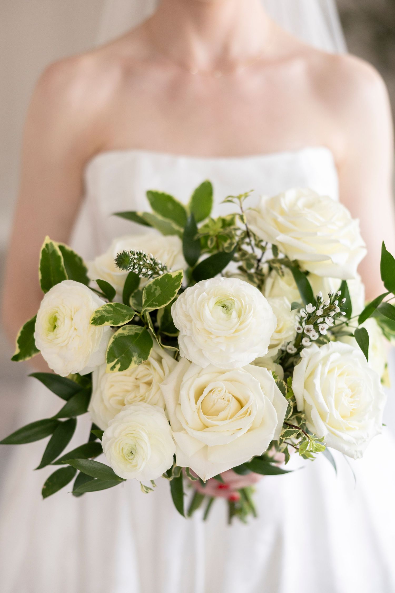 Elegant white rose and greenery bouquet displayed against wedding dress bodice.