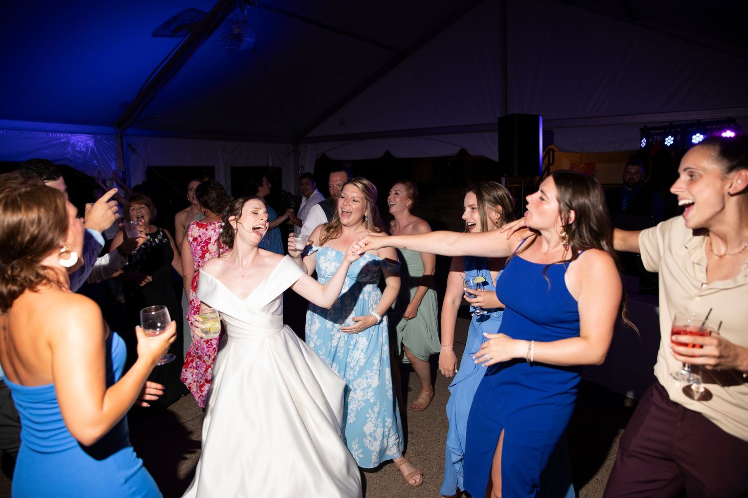 Crowded dance floor with wedding guests dancing under blue lighting.