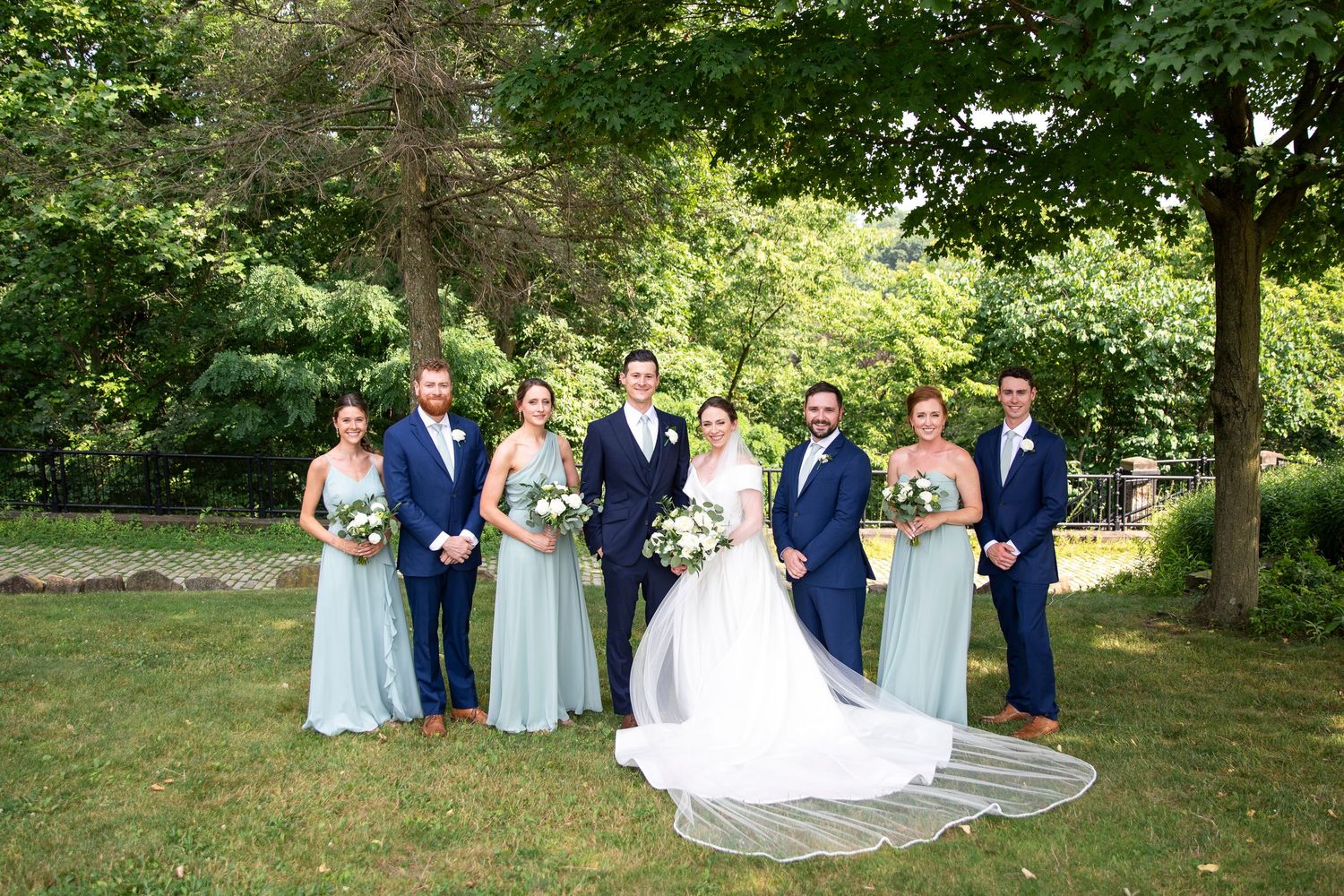 Wedding party in navy and light blue attire poses together on a lush green lawn.