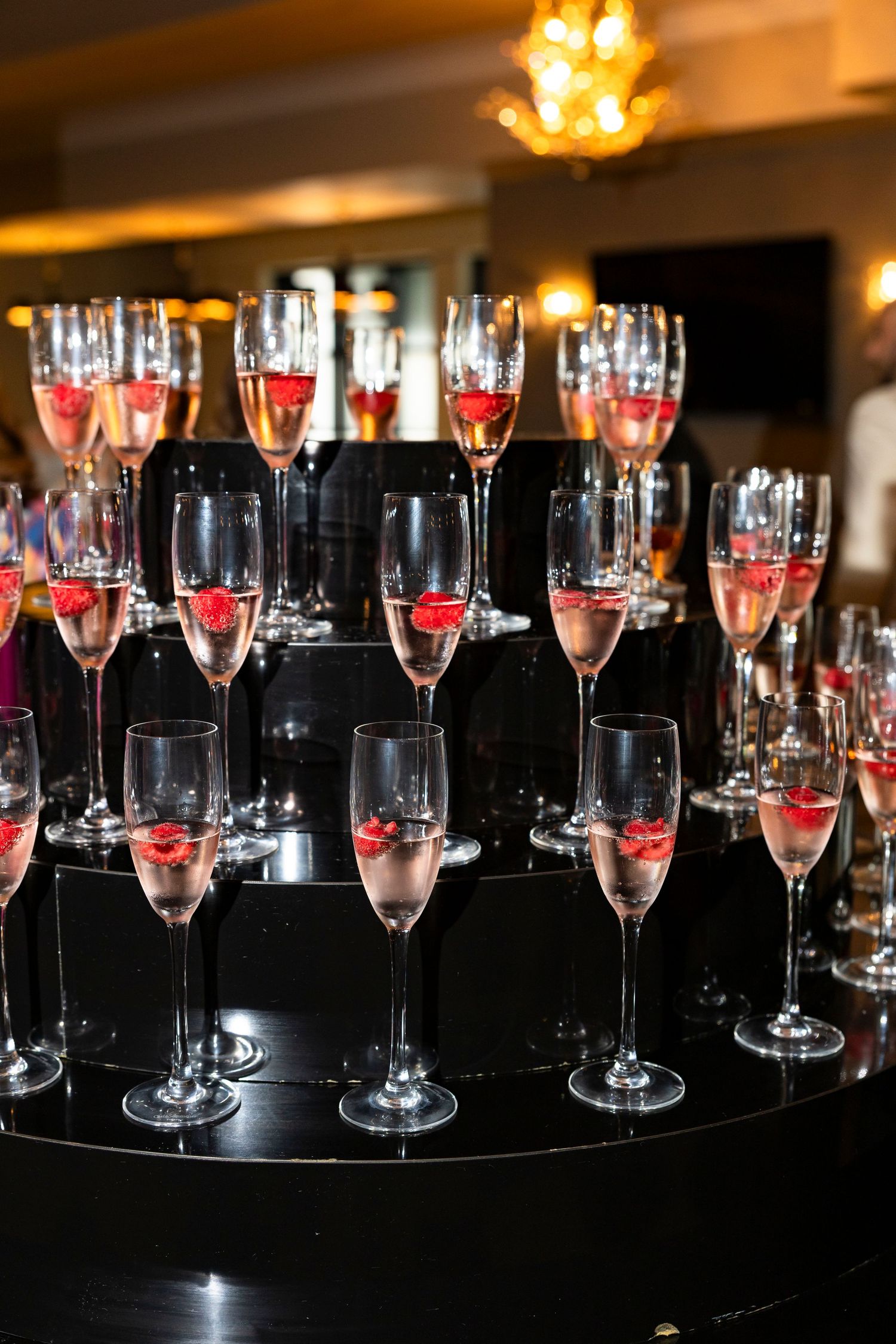 Rows of champagne glasses arranged on dark reflective surface with warm lighting.