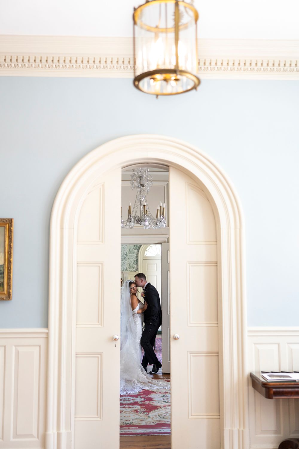 Bride and groom share a romantic moment framed by an elegant arched doorway in a classic blue wedding venue.